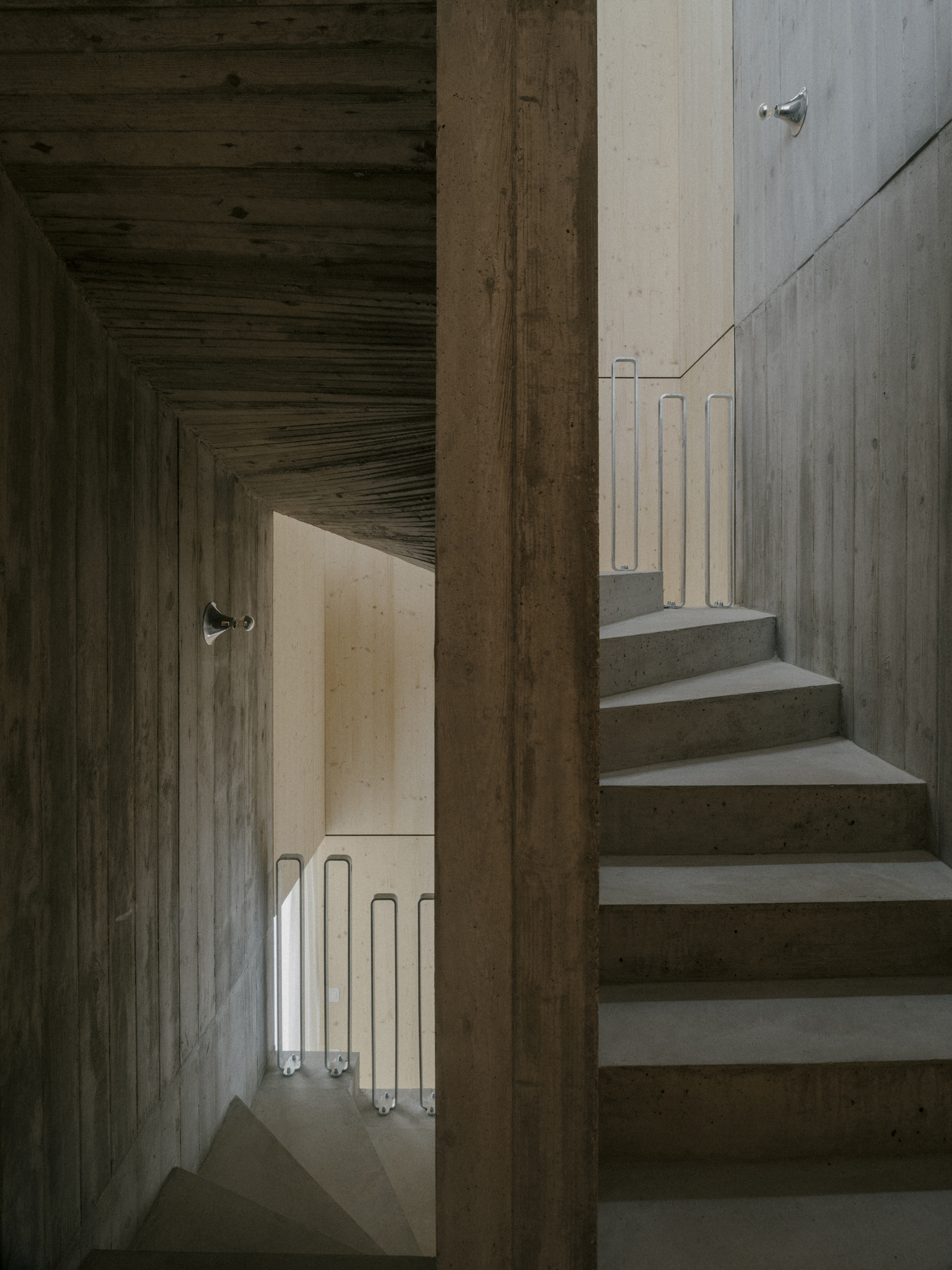 View through timber doorway showing concrete stairs ascending alongside a corridor with tube lighting below