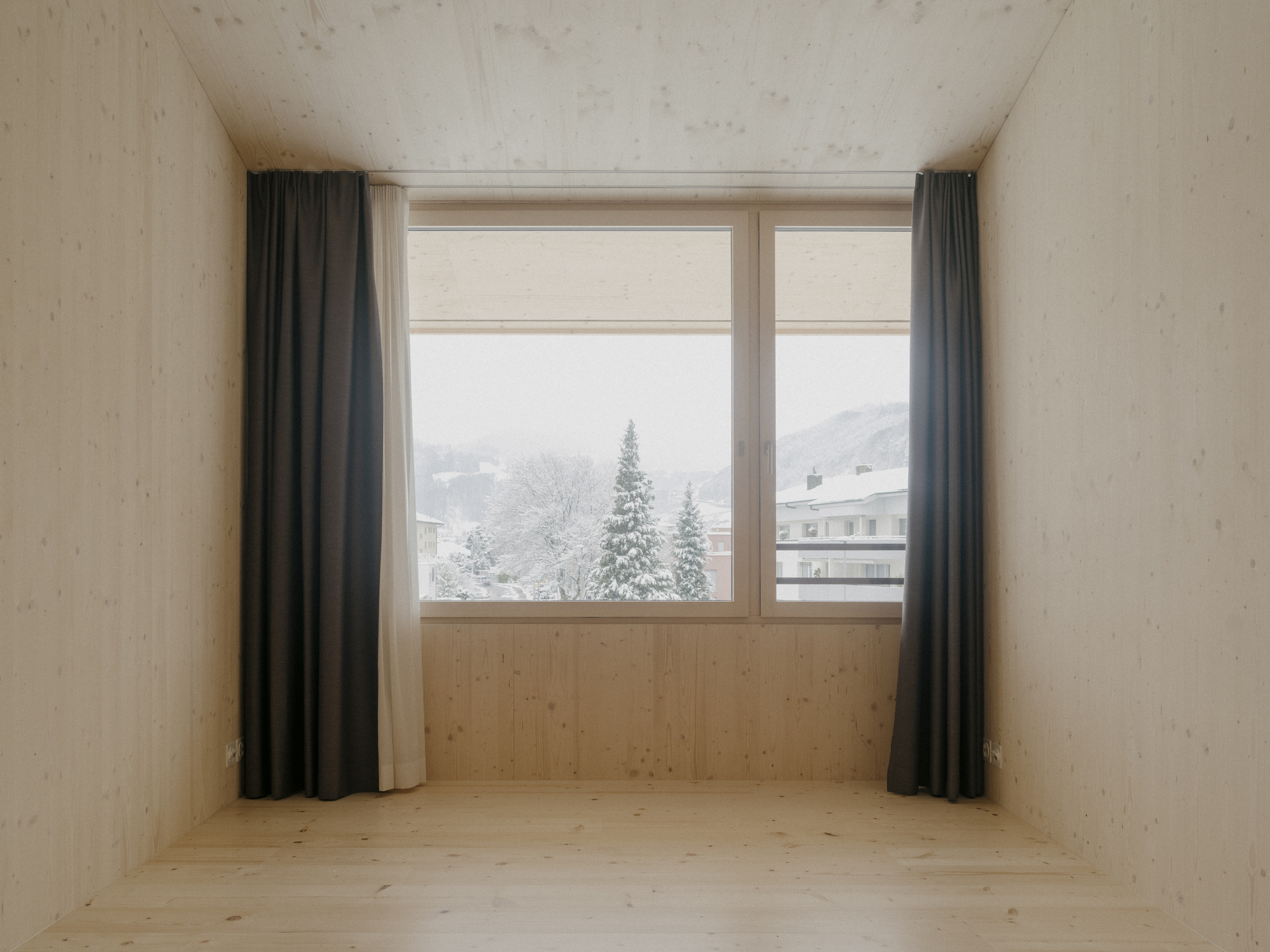 Window alcove framed in timber with view to snow-covered conifers and alpine landscape beyond