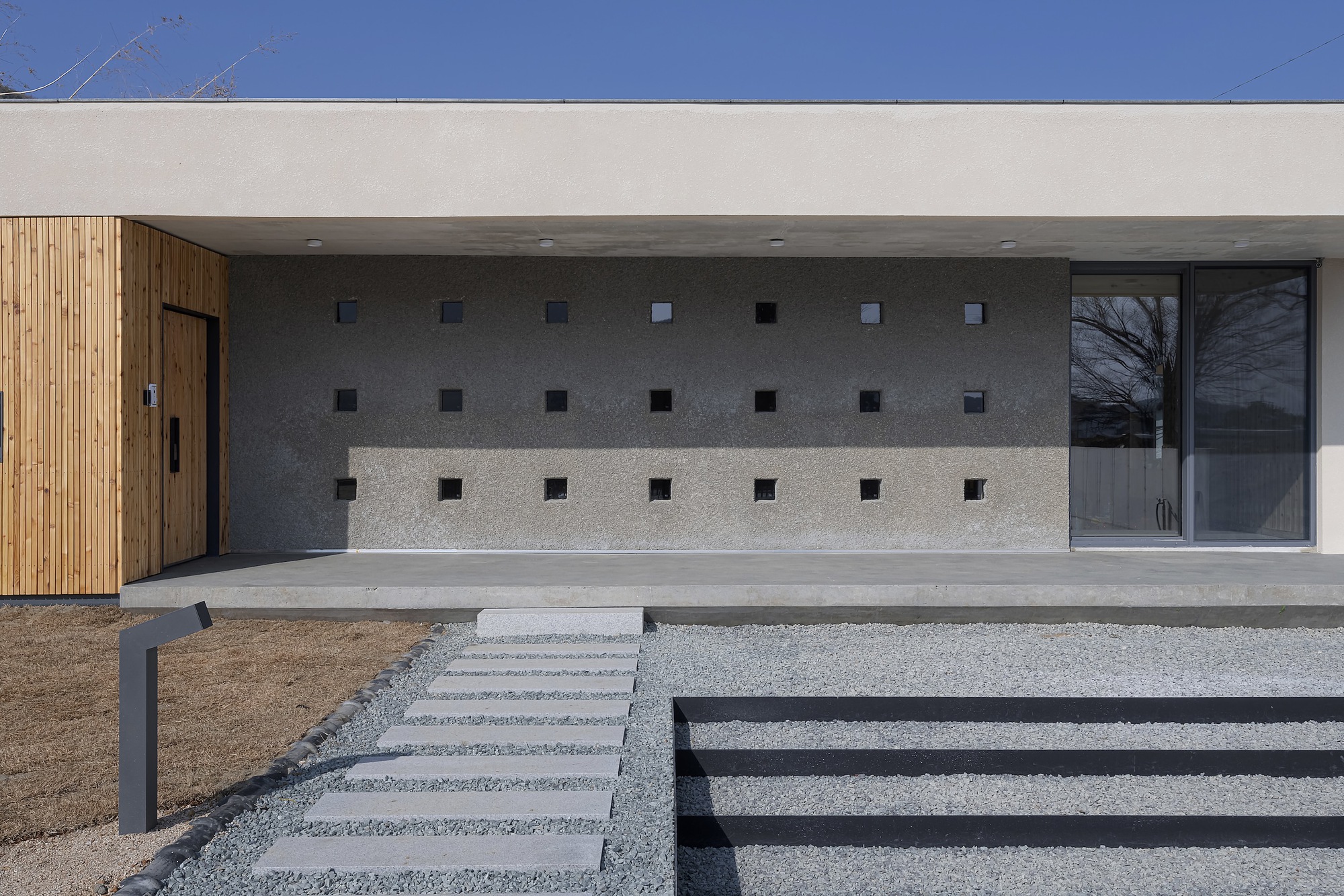 Facade with grid of square openings in concrete wall flanked by timber cladding and glazing
