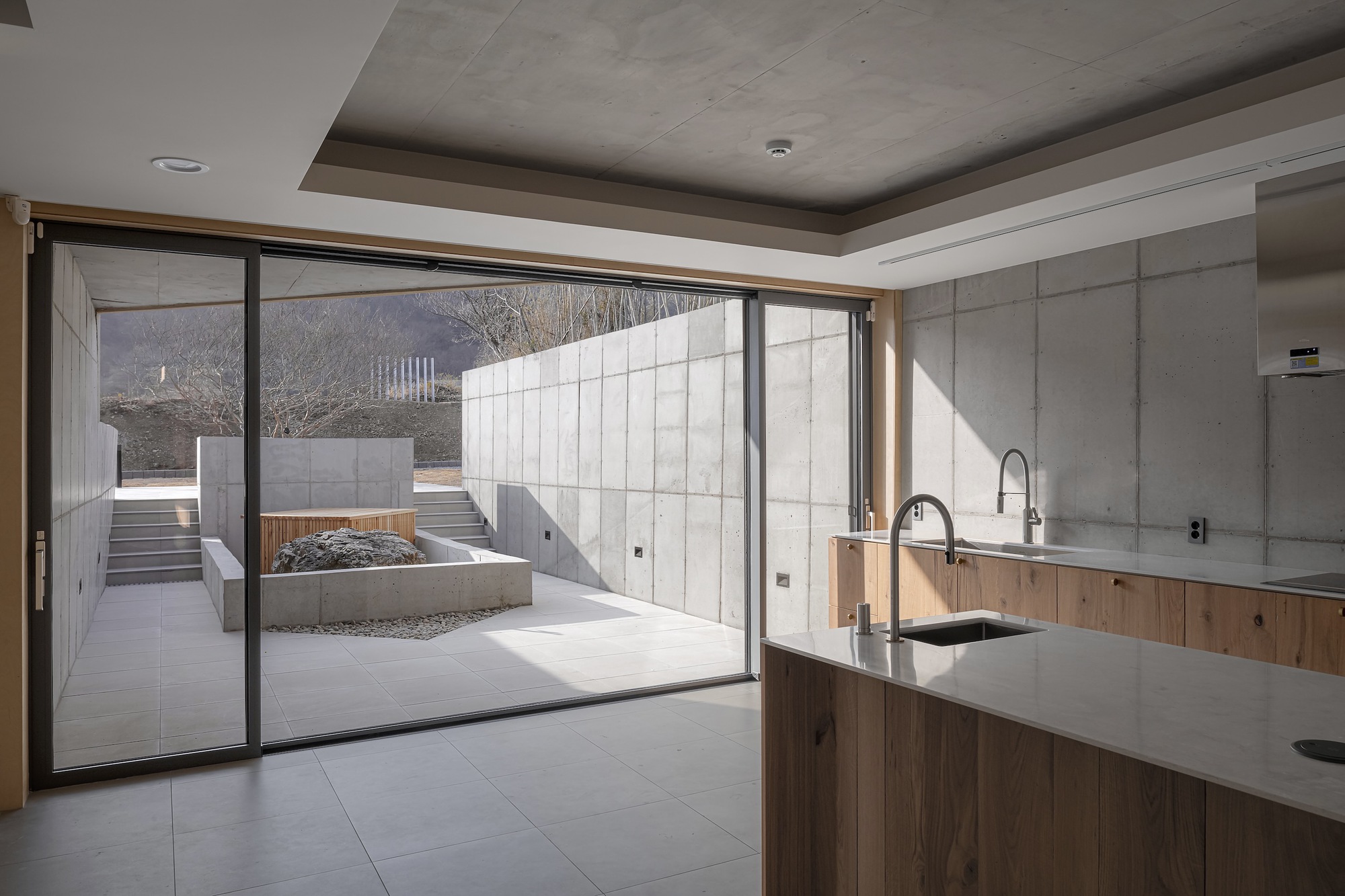 Kitchen with timber cabinetry and concrete walls opening to courtyard through sliding glass doors