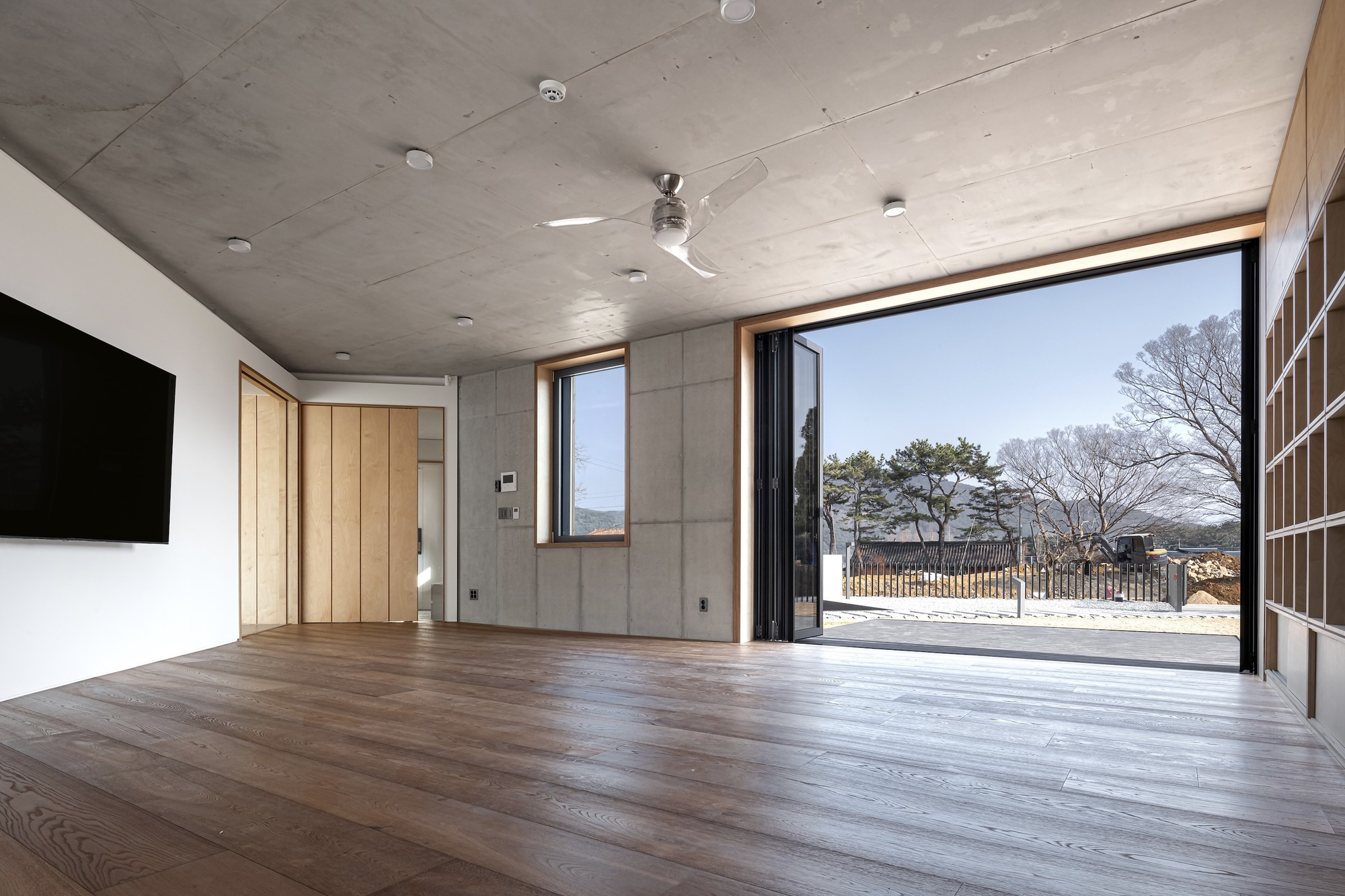 Living room with wide timber flooring and concrete ceiling opening to a courtyard through full-height glazed doors