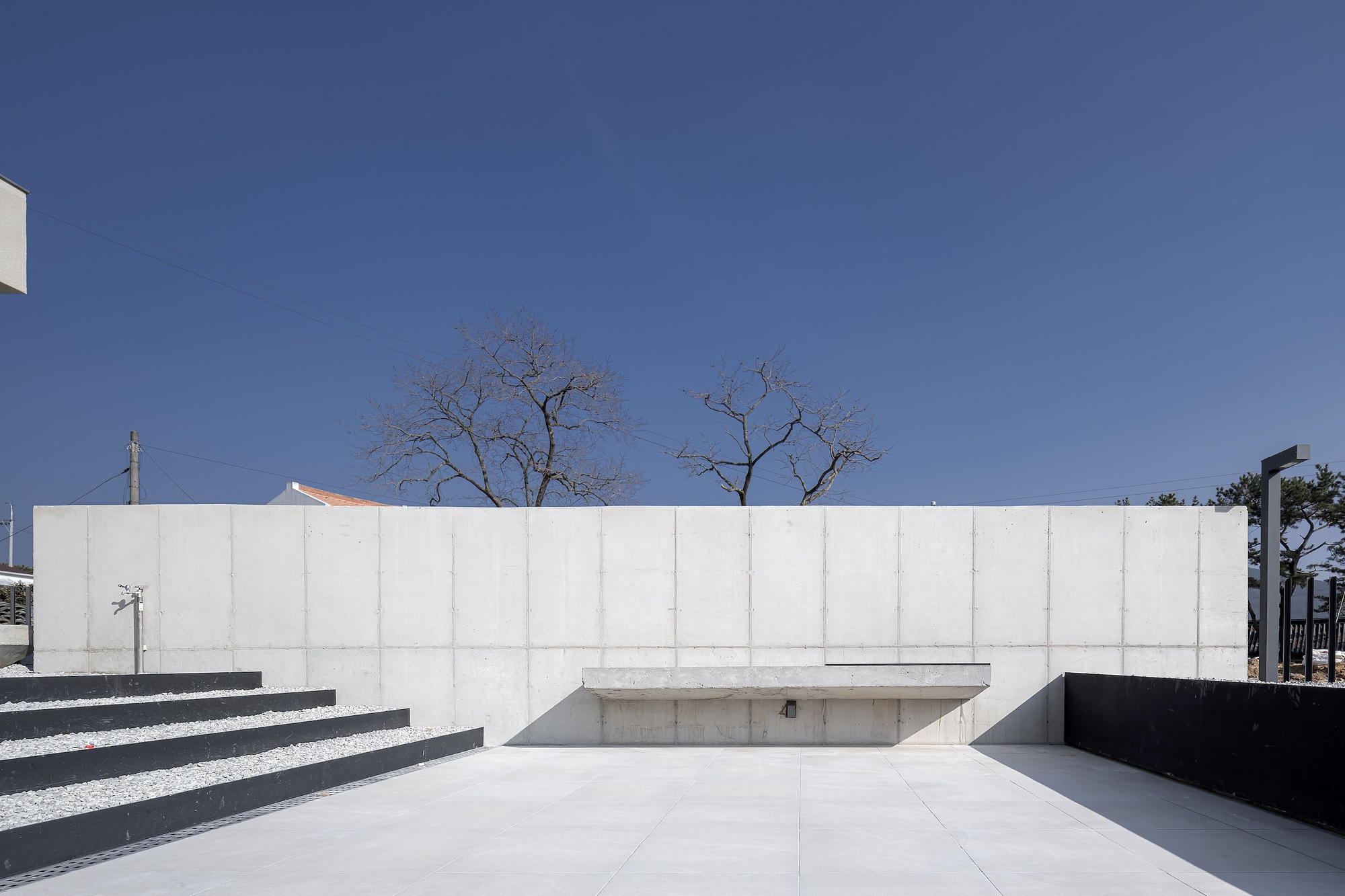 Concrete courtyard wall with recessed steps and sunken pool area beneath bare winter trees