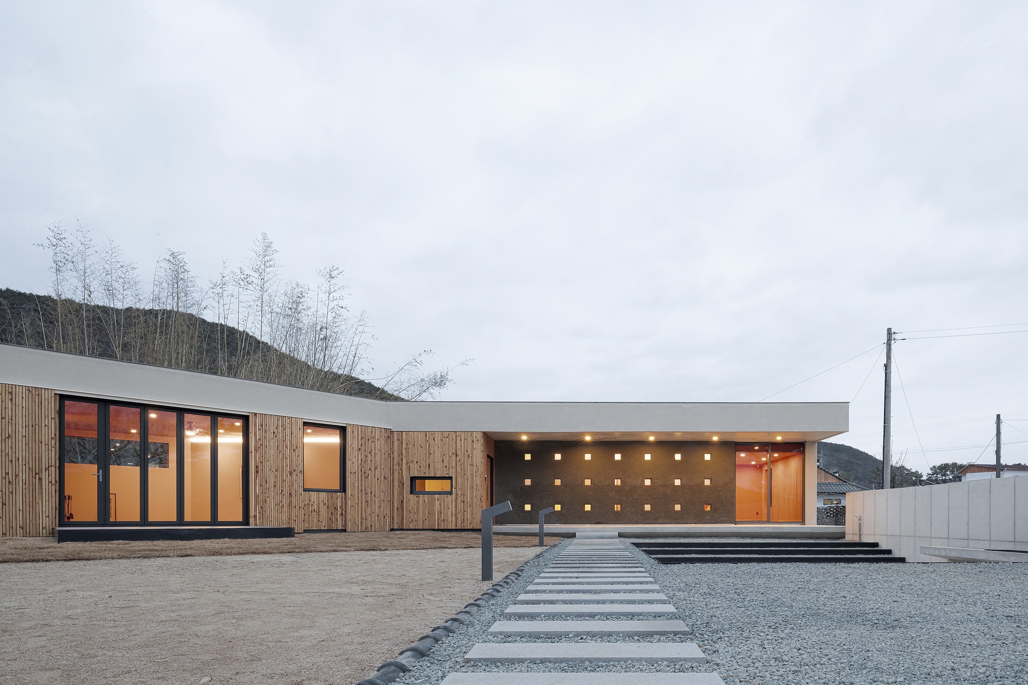 Horizontal facade combining timber cladding and white concrete with recessed square openings at dusk
