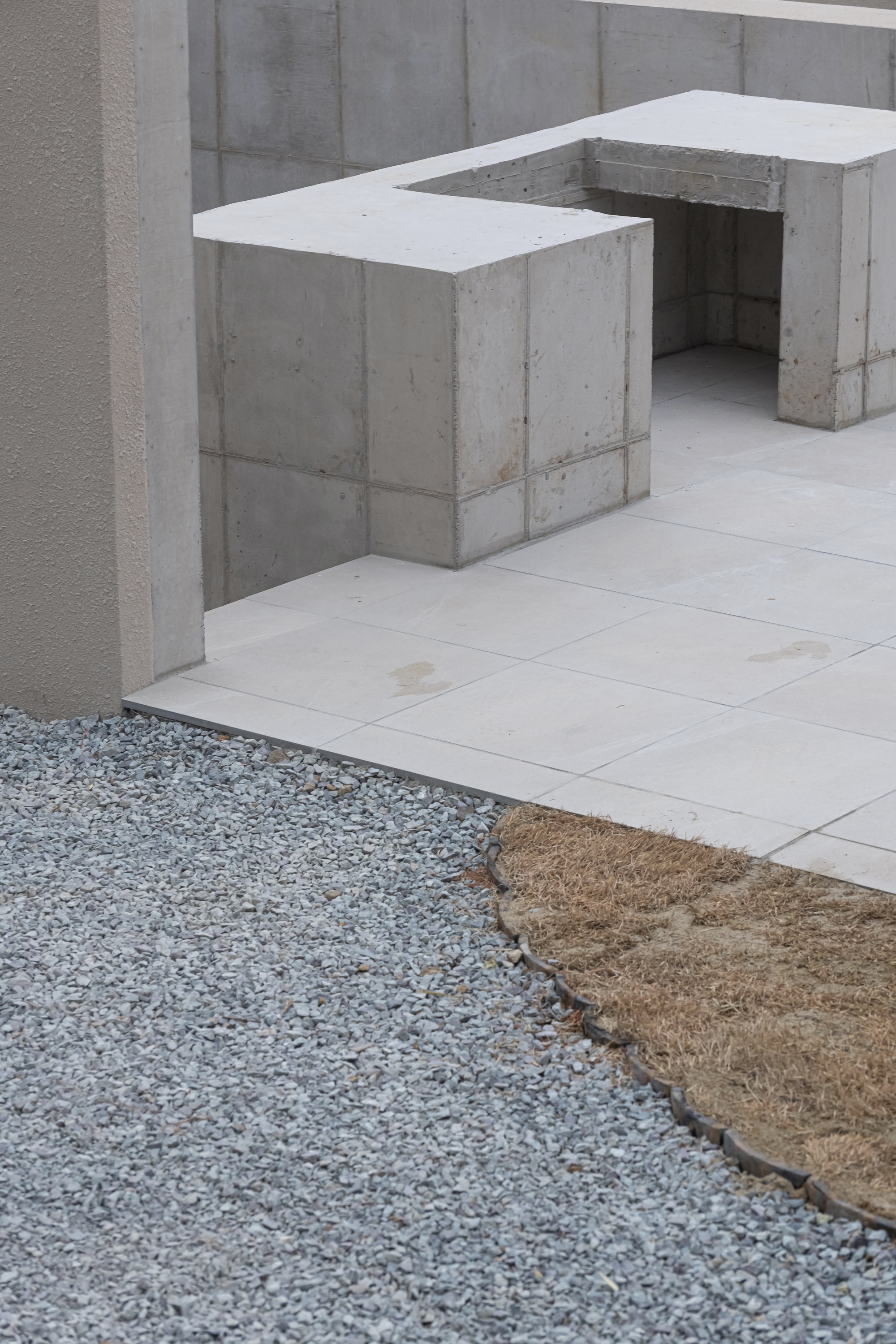 Board-formed concrete seating elements flanking gravel and paved stone ground plane