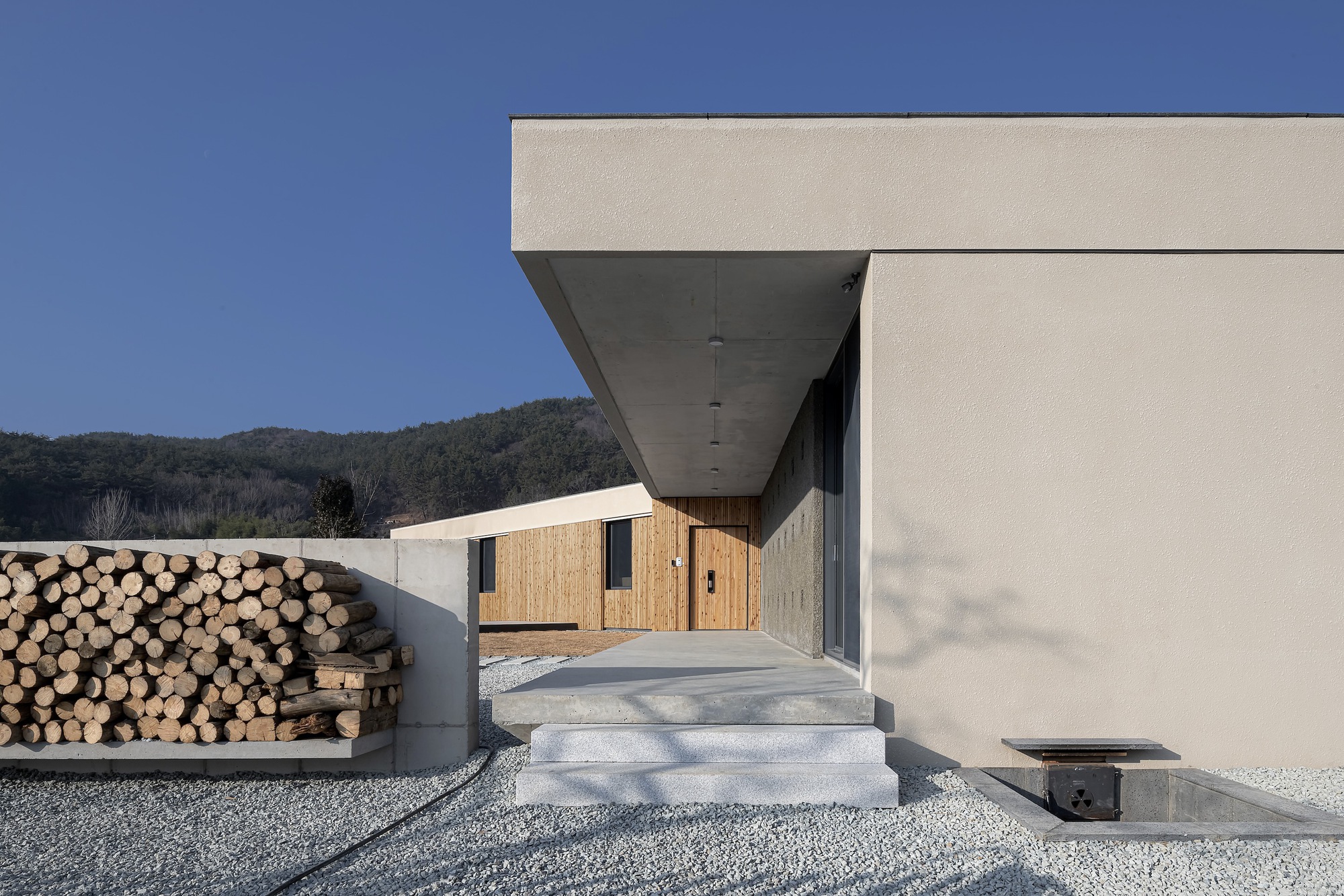 Entry steps leading to recessed entrance with stacked firewood wall and distant timber building