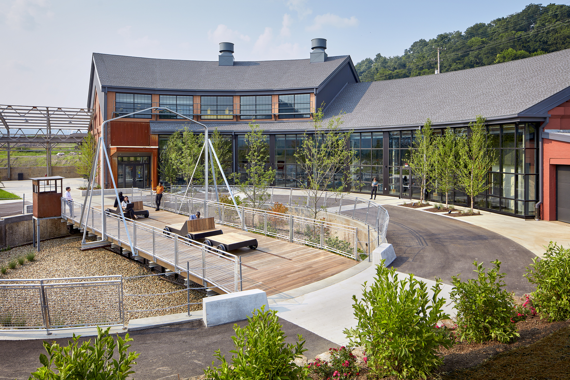 Elevated terrace with timber decking and cable railings, planted beds with young trees and swings between metal frames