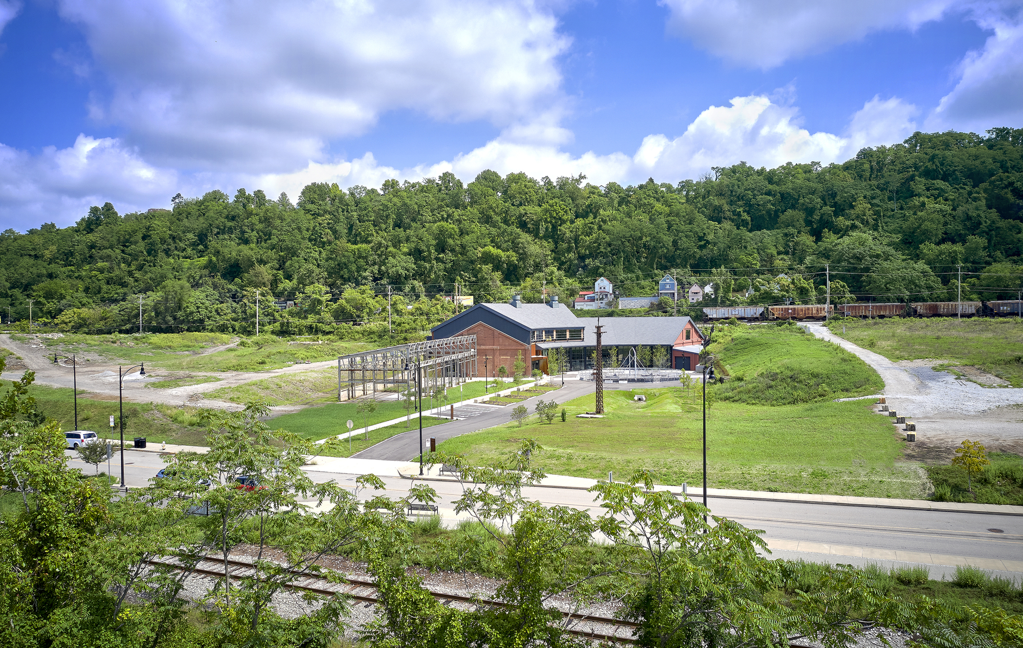 Wide view of the campus set in a green valley with young trees lining the access road and wooded hillside beyond