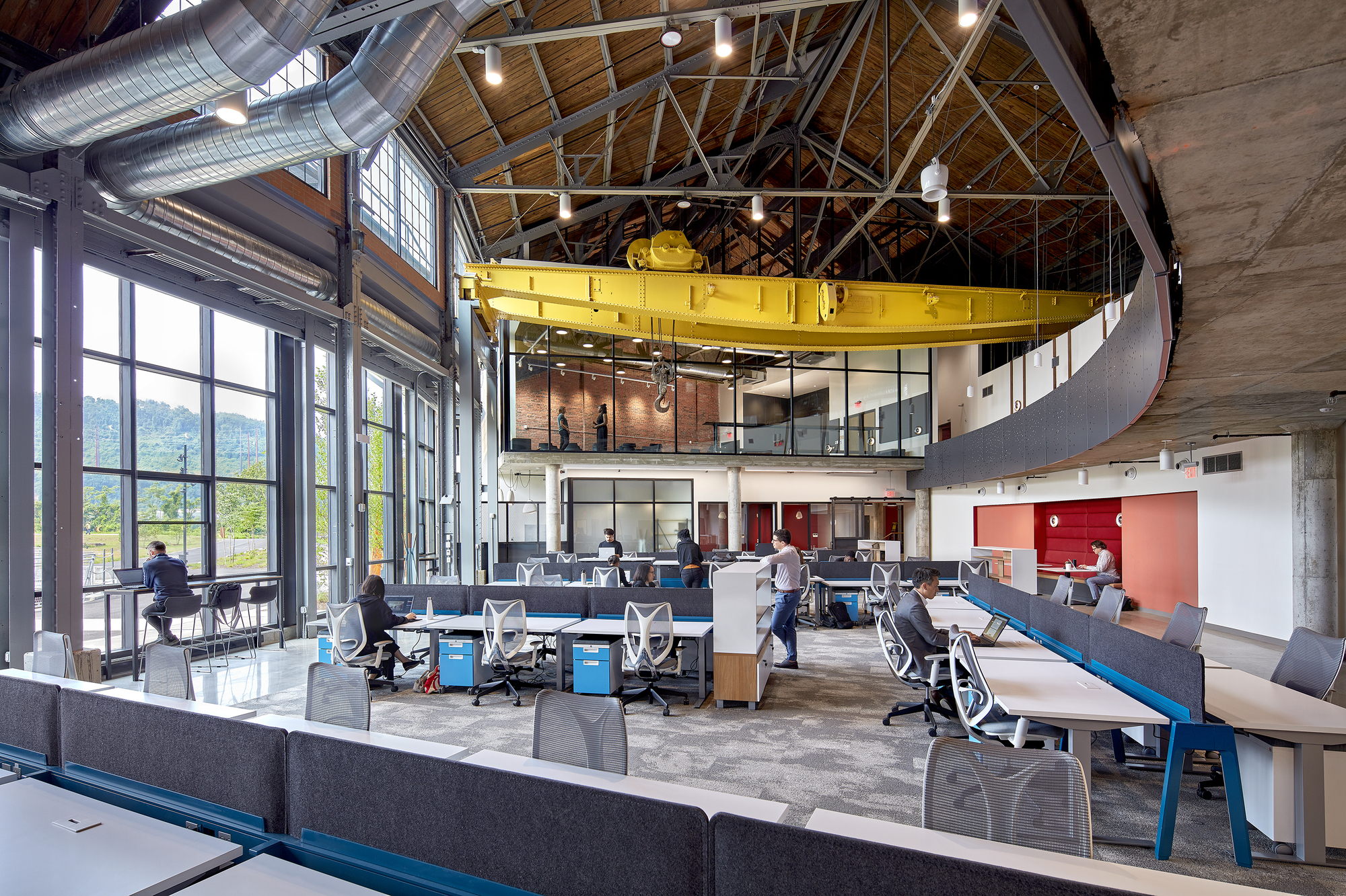 Multi-level interior with yellow suspended crane structure above workstations and conference rooms under exposed timber trusses