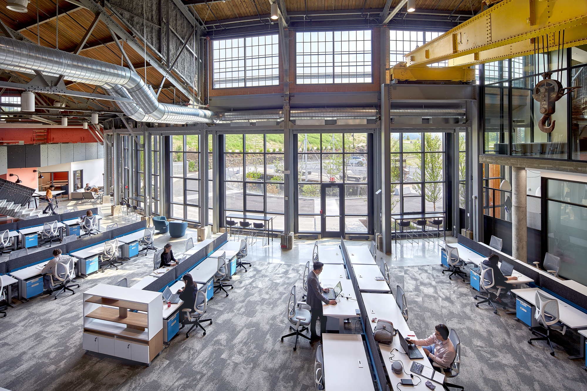 Double-height workspace with exposed timber roof trusses, steel columns, and rows of desks below clerestory windows