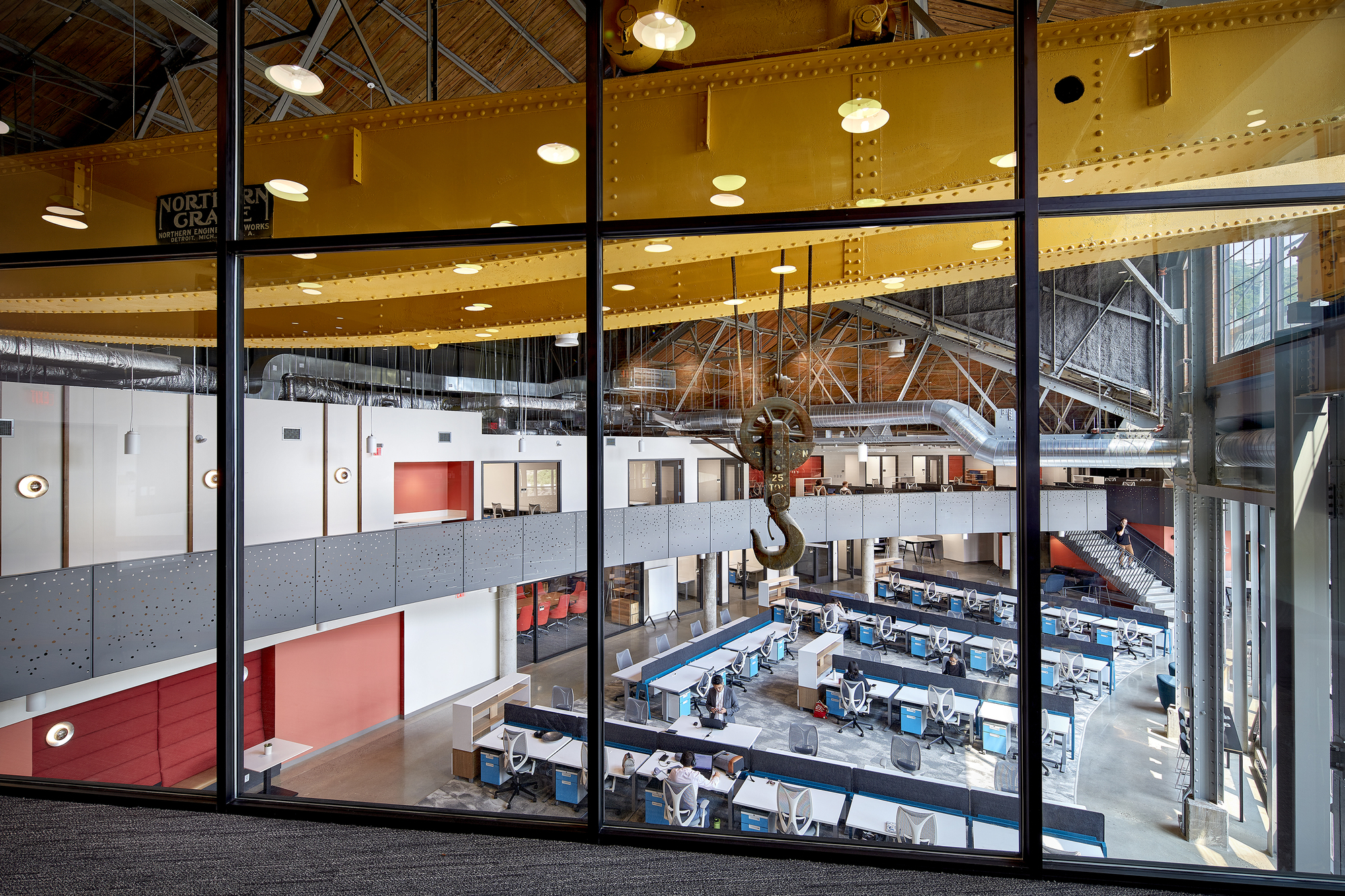 View through glazed partition wall overlooking the open workspace and yellow-painted crane beam at upper level