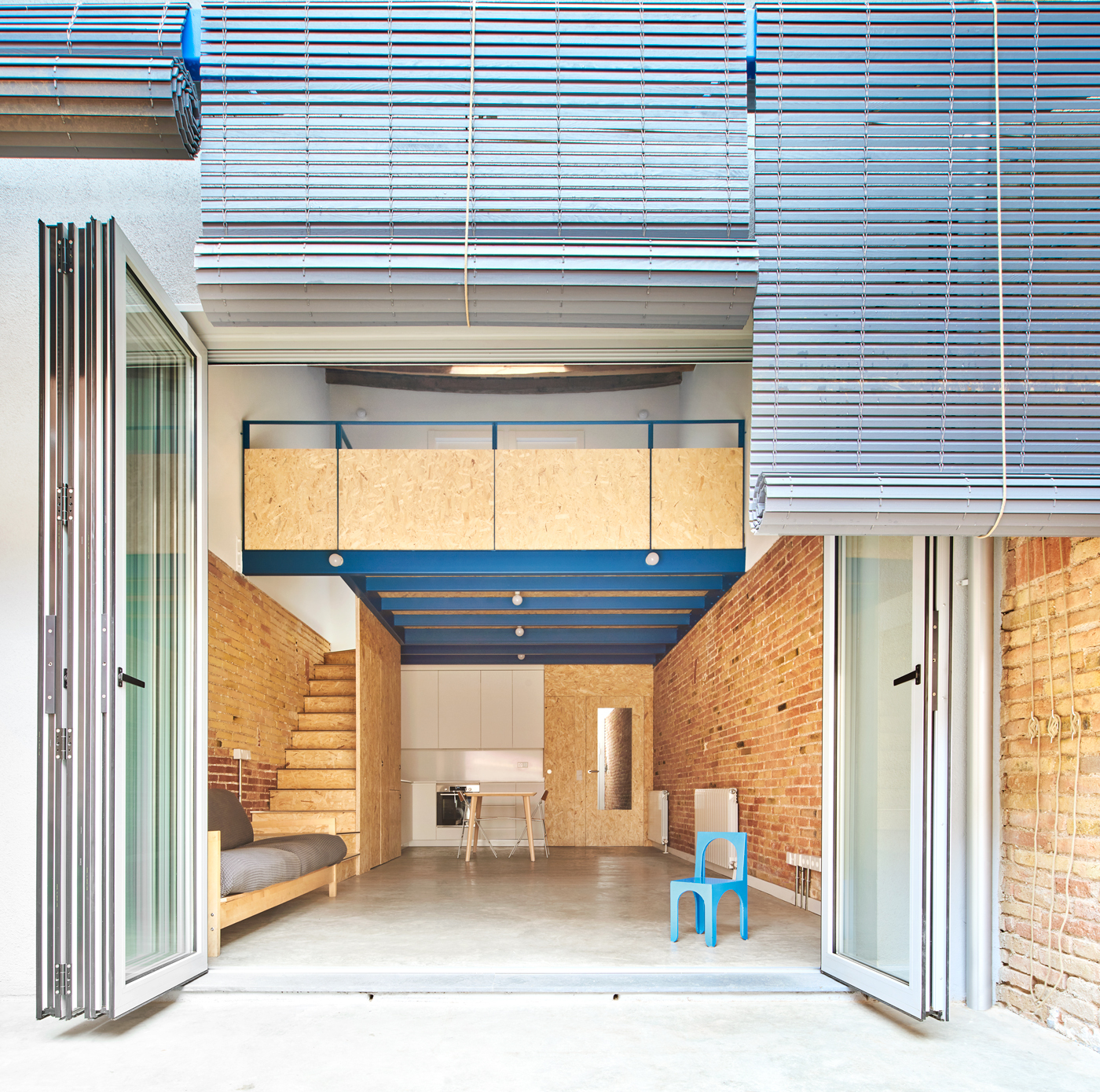 View from courtyard through open folding doors to blue steel mezzanine beneath metal louvered canopy