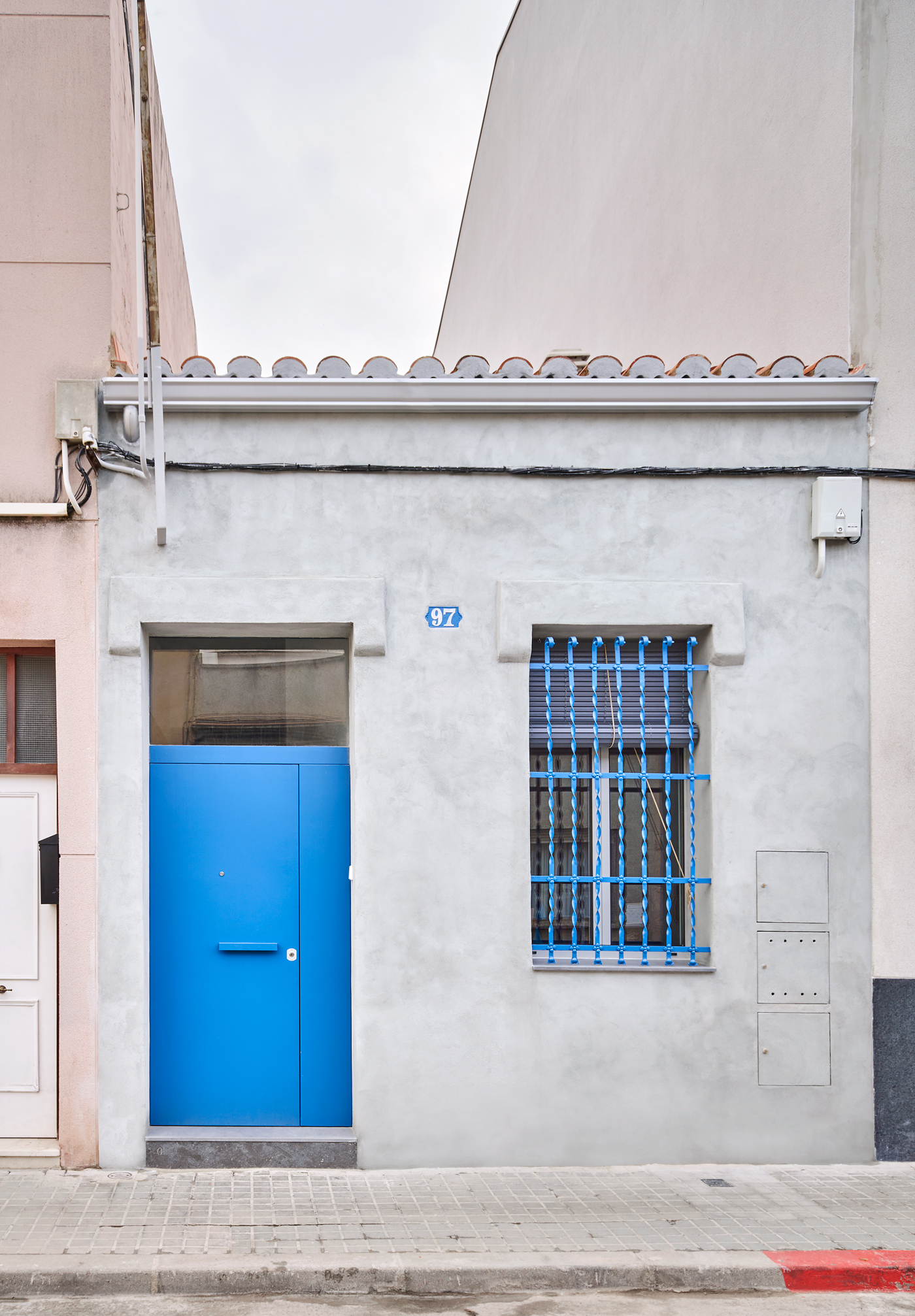 Street facade with bright blue door and barred window on a white stucco wall