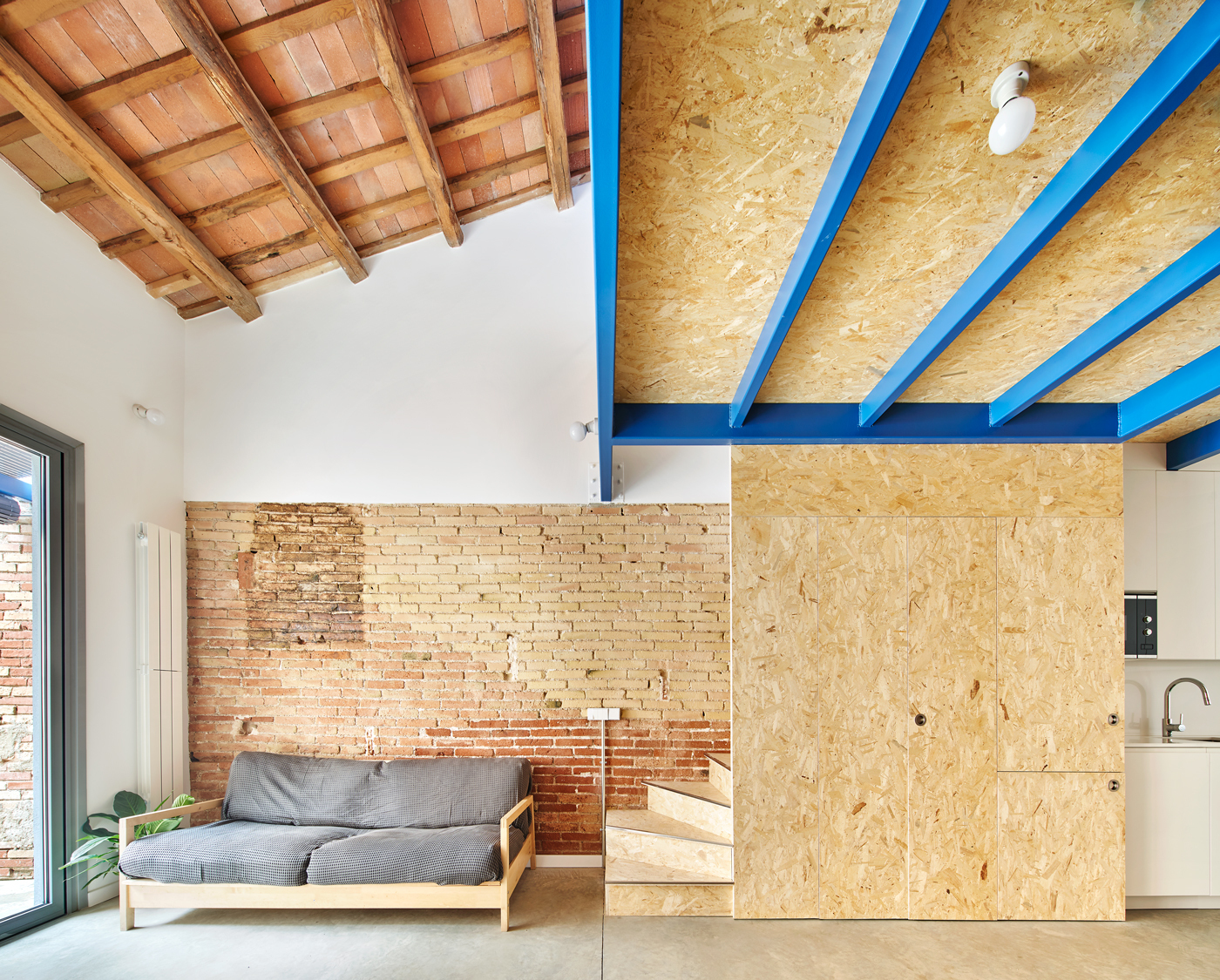 Interior living space with exposed brick wall and oriented strand board ceiling panels on blue joists