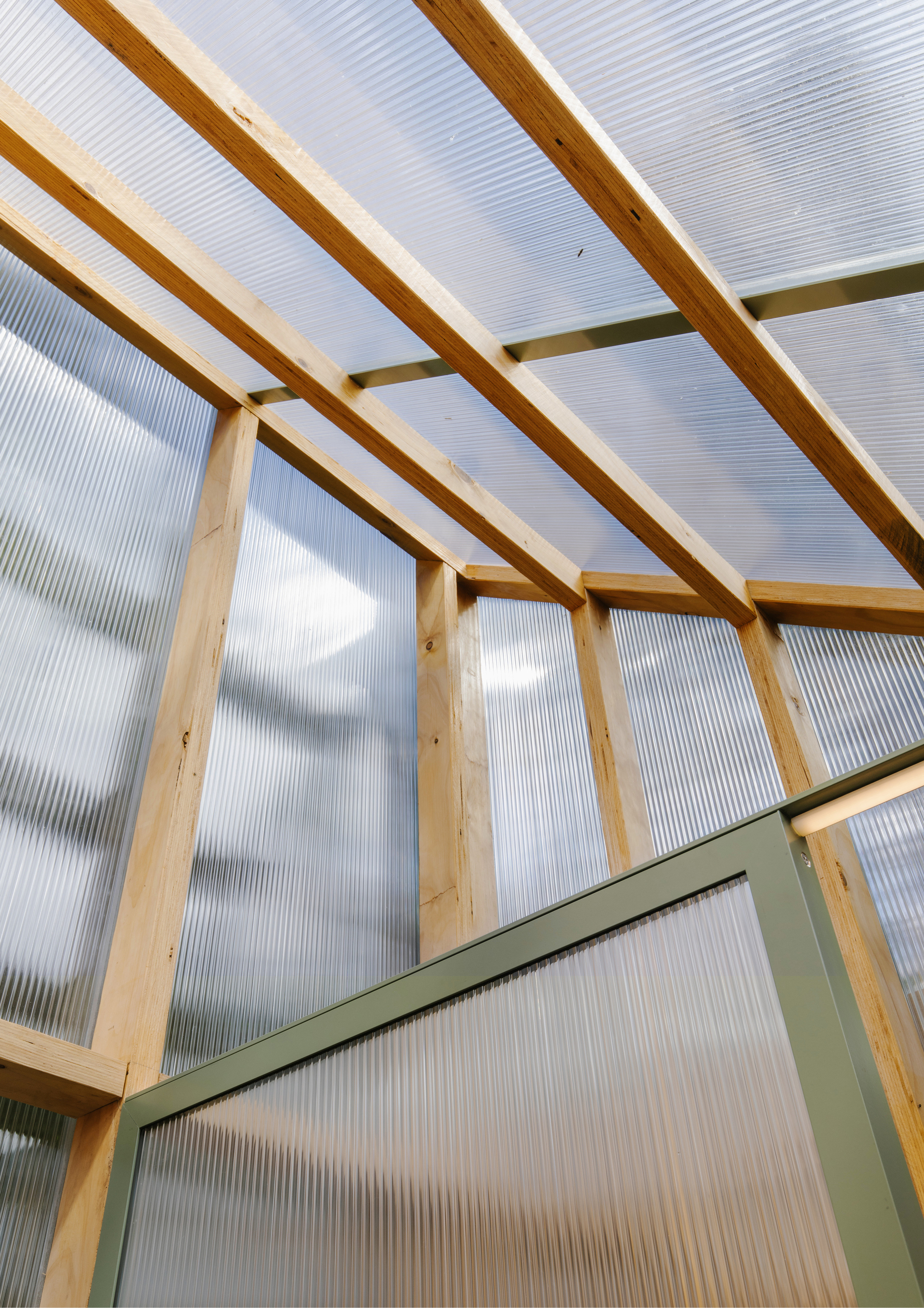 Sloped ceiling with exposed timber rafters and translucent corrugated polycarbonate panels under clouds