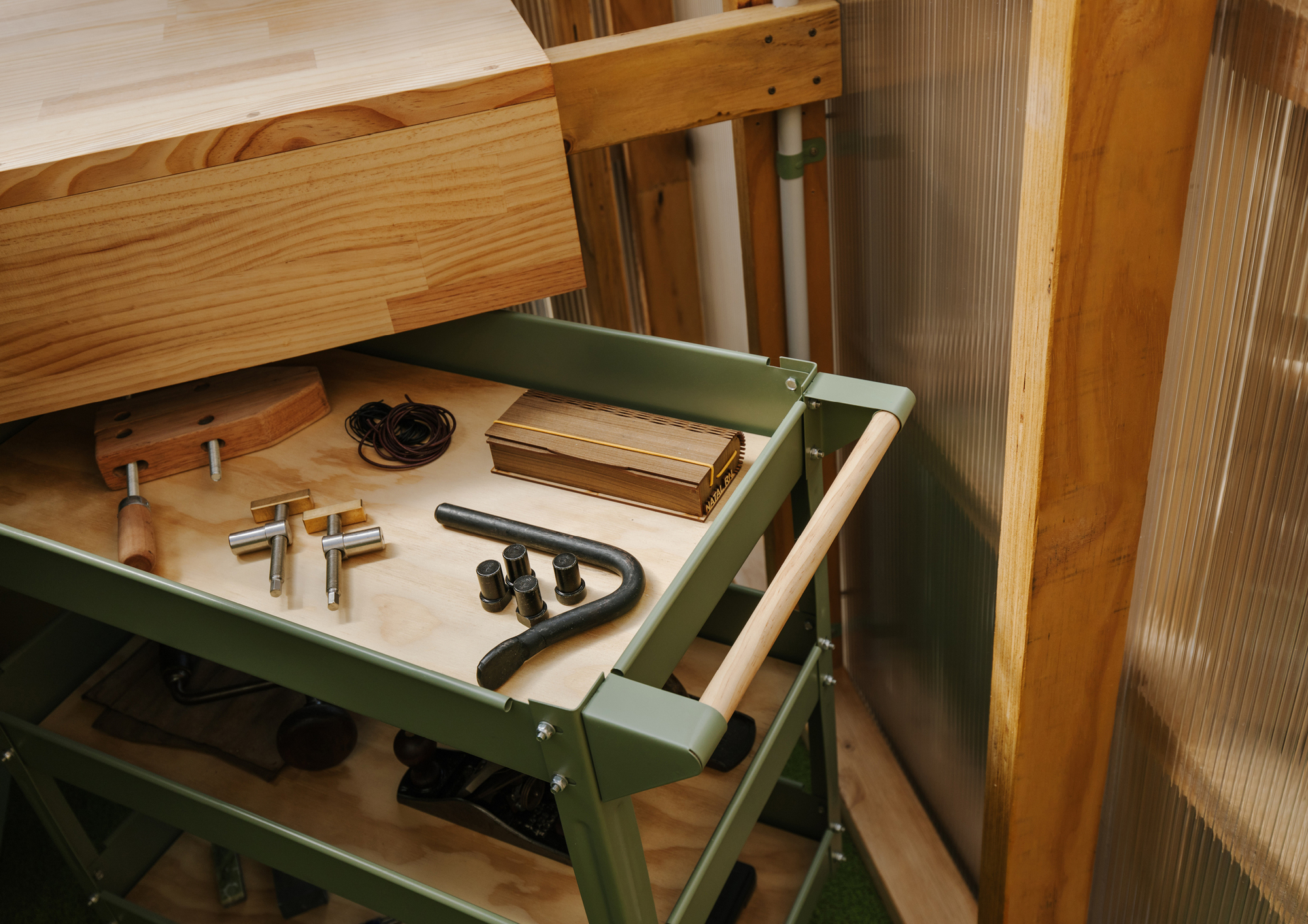 Open drawer of green metal tool cart displaying hardware and hand tools on plywood base
