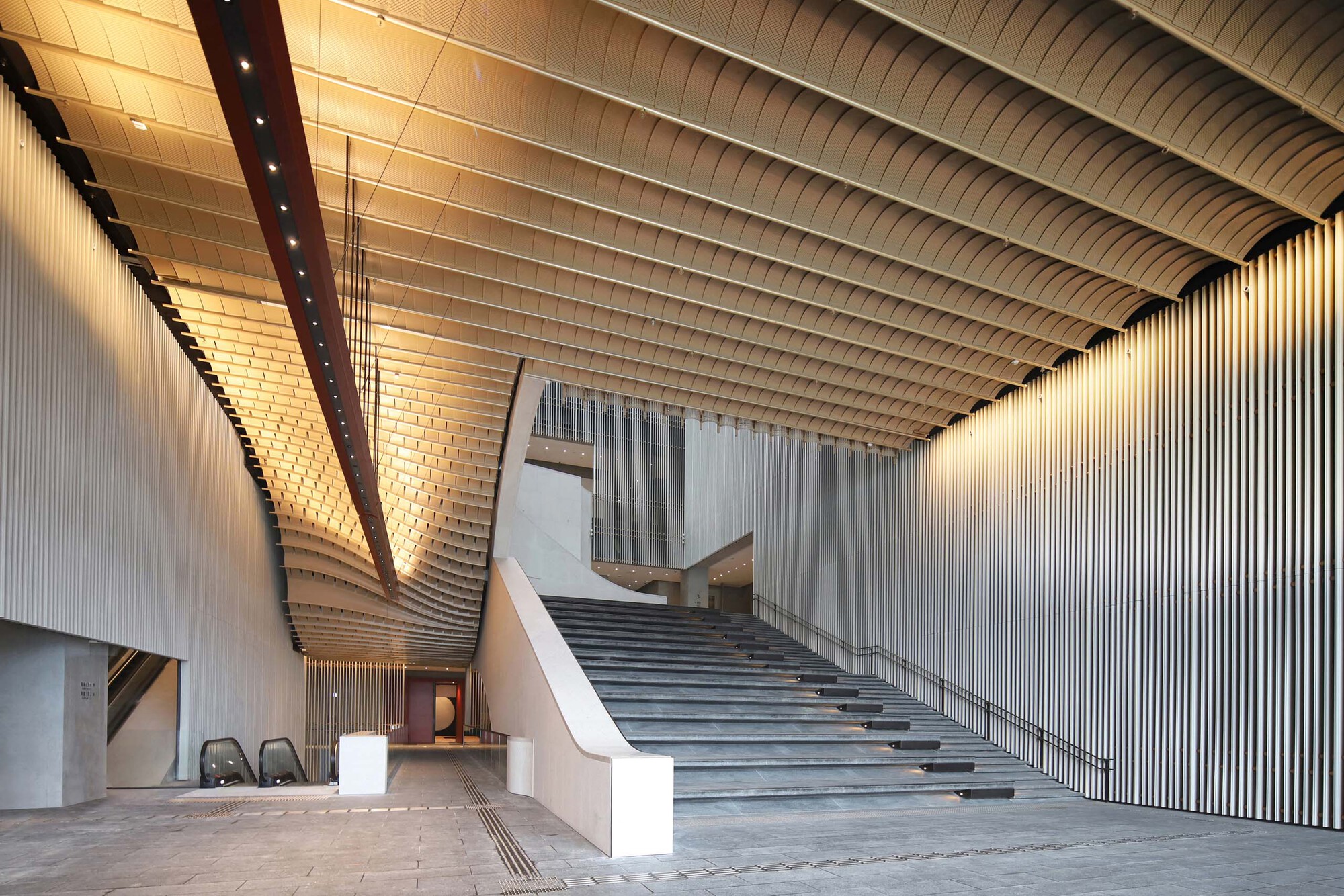 Interior lobby with curved horizontal ceiling panels and a wide staircase ascending to upper levels