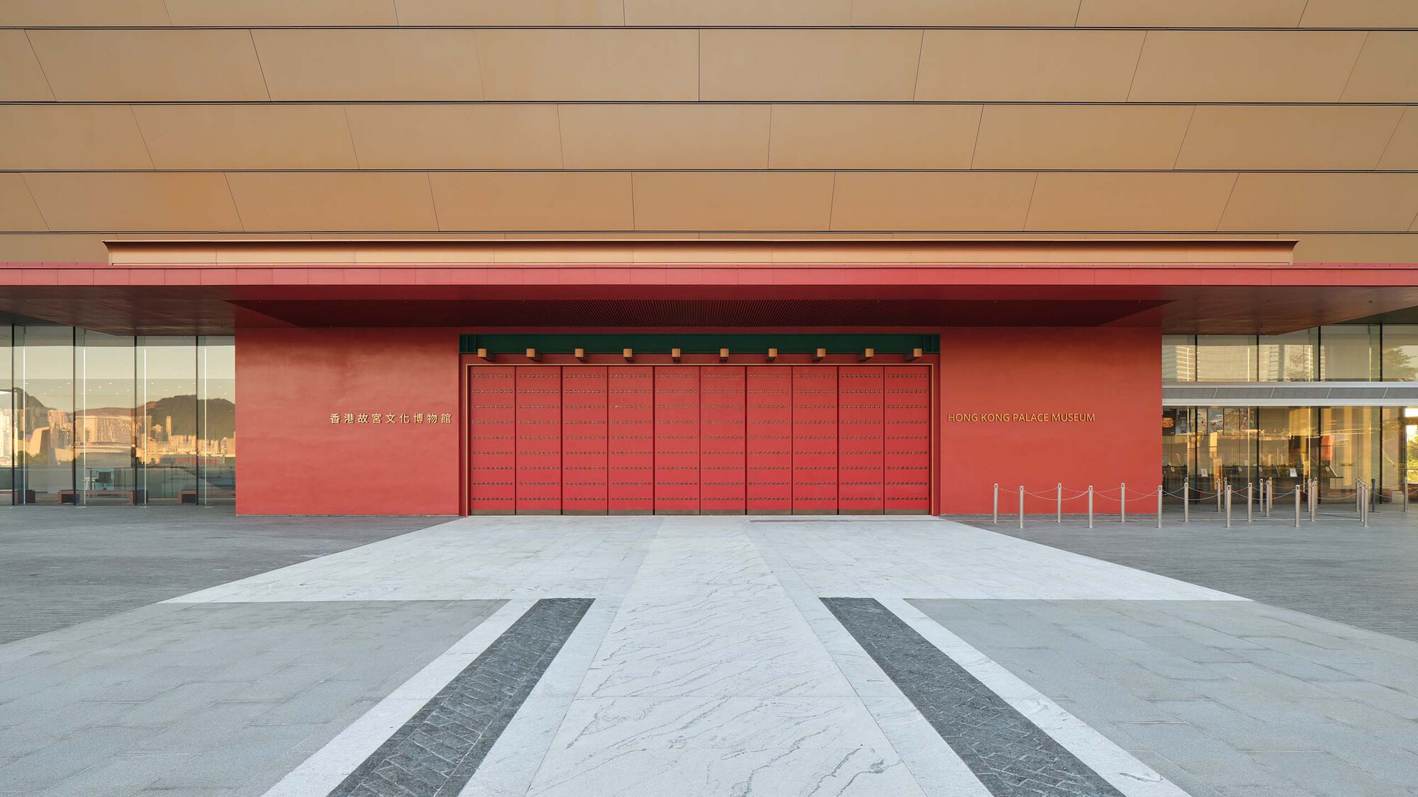 Entrance plaza with red folding doors and striped paving beneath a beige canopy