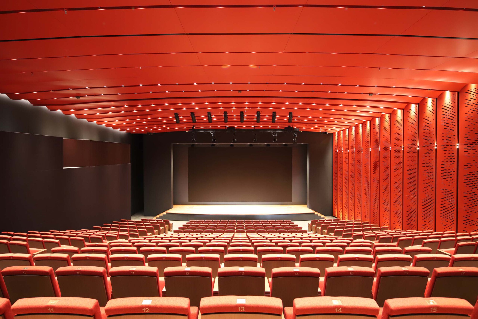 Auditorium interior with textured red acoustic ceiling panels and matching upholstered seating facing the stage
