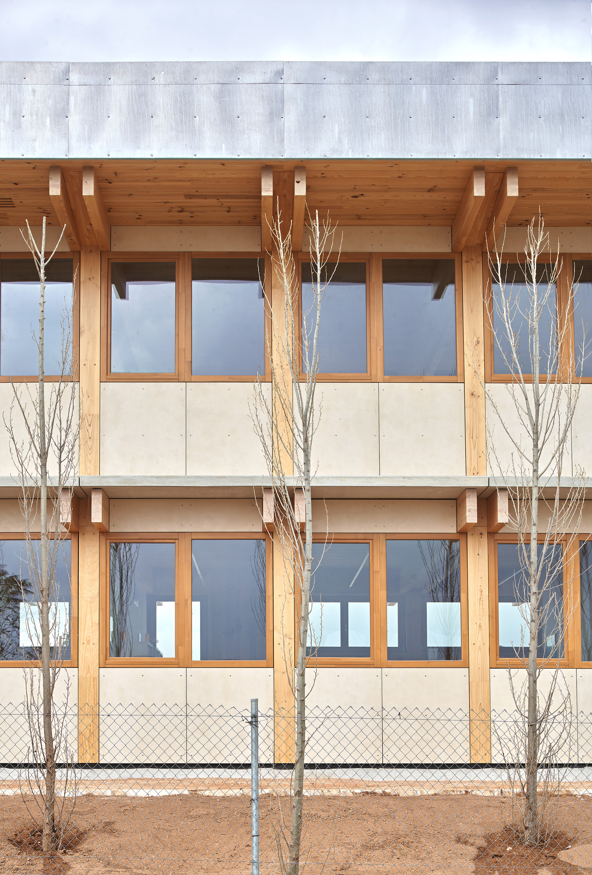 Two-story timber facade with horizontal banding and bare winter trees behind chain-link fence