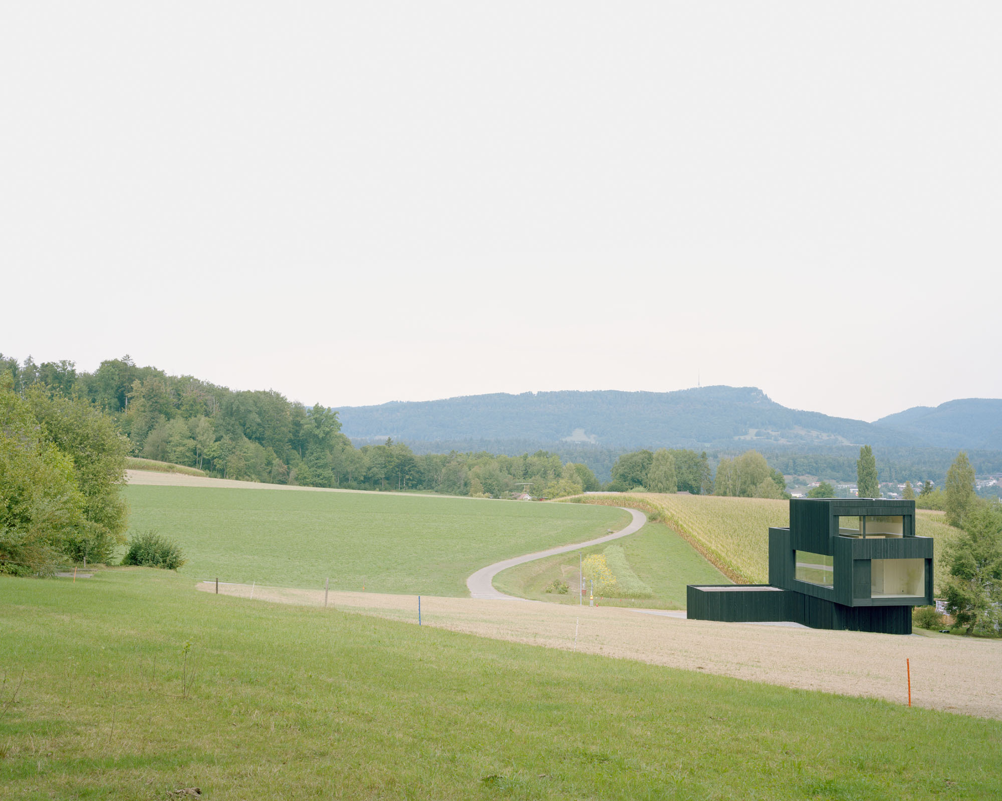 Distant view of the rectilinear volumes positioned beside a winding road through rolling green hills