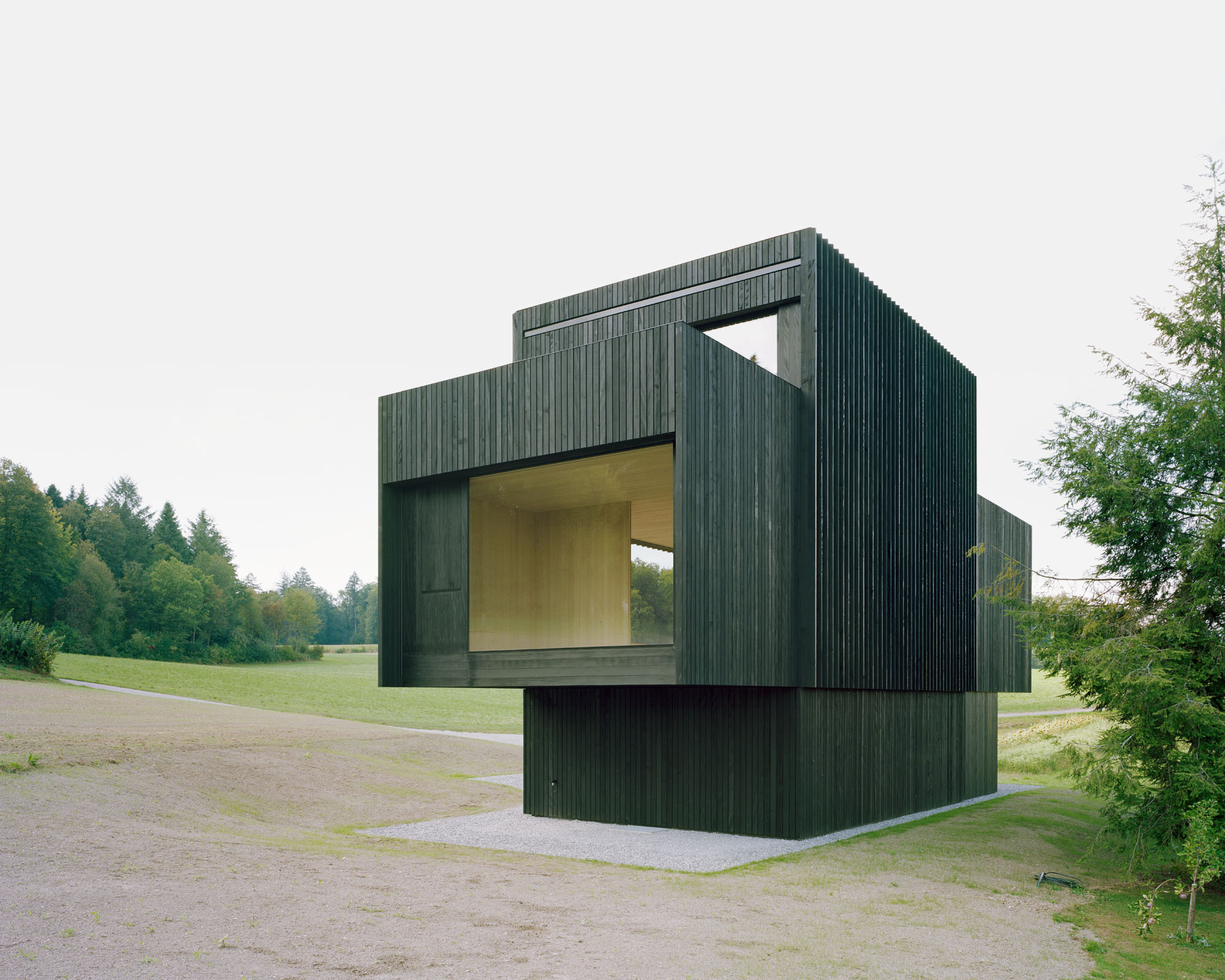 Corner elevation showing vertical timber cladding with deep recessed openings revealing interior volumes