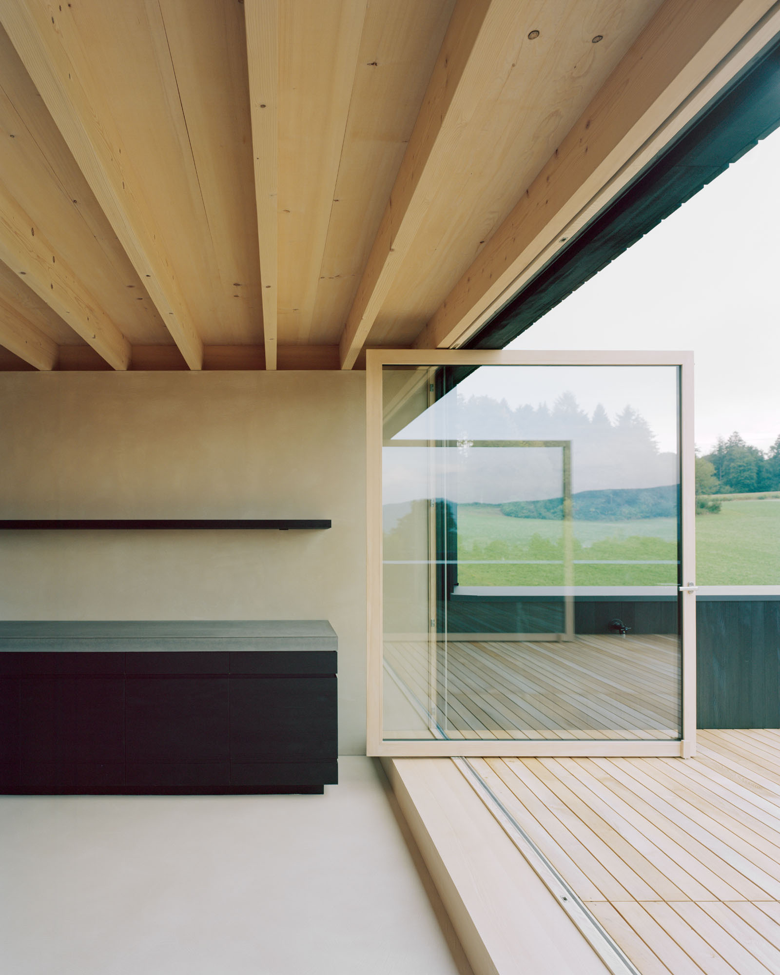 Interior view through glass wall to exterior deck with exposed timber ceiling joists above