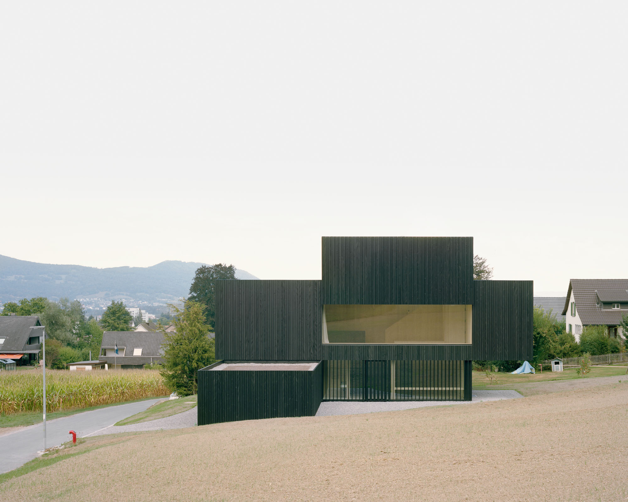 Dark ribbed timber volumes with horizontal yellow glazing set among roads and residential rooftops