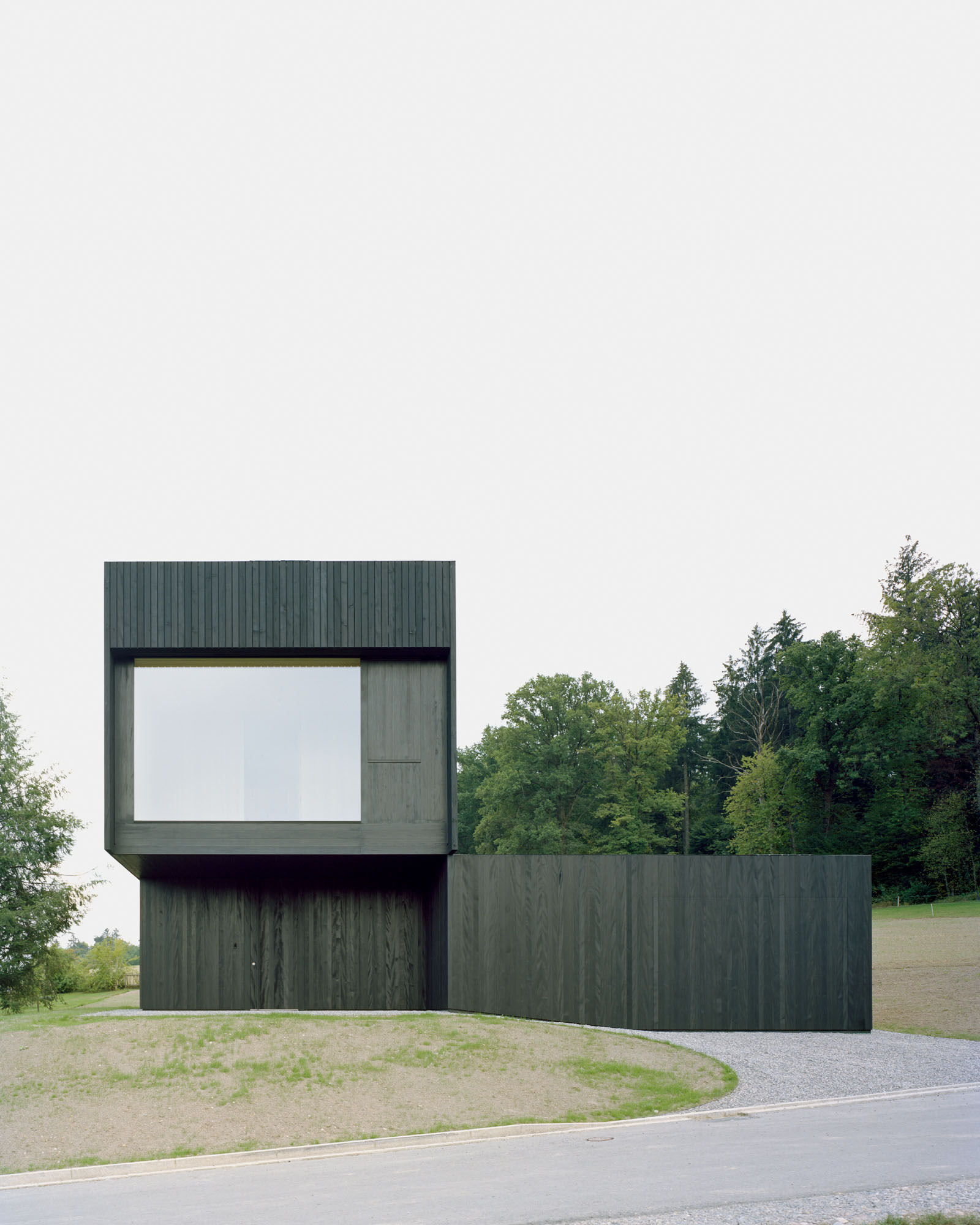 Cantilevered volume with large square window opening clad in blackened vertical wood siding