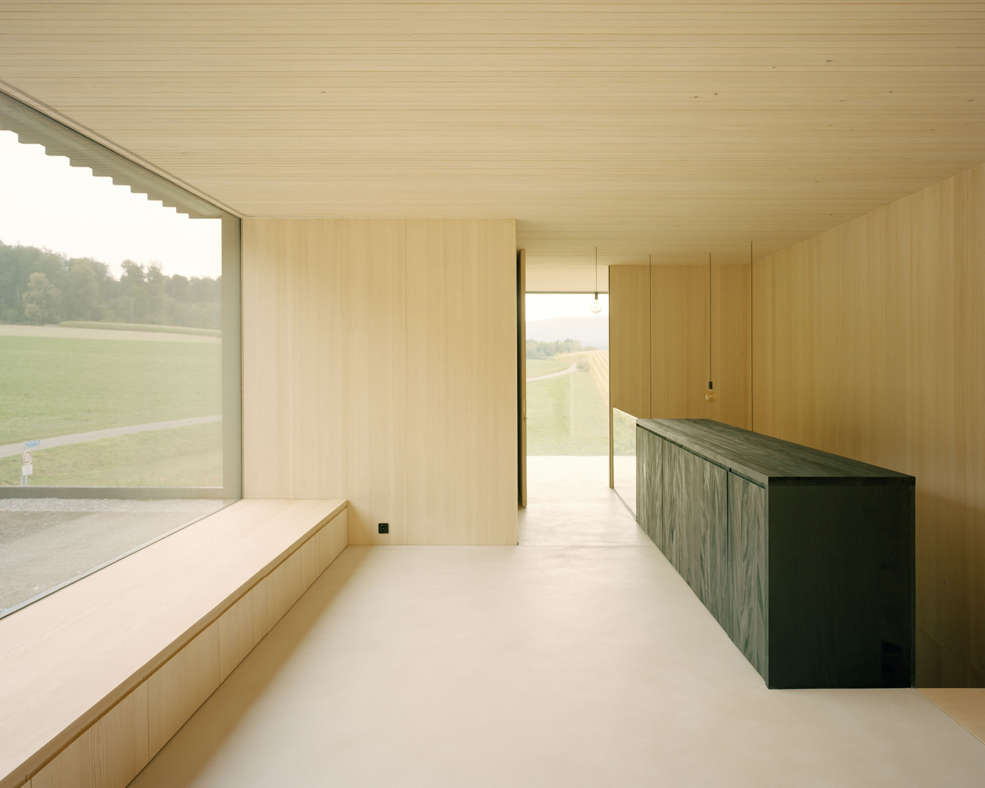 Plywood-lined room with built-in bench and dark cabinetry overlooking open fields