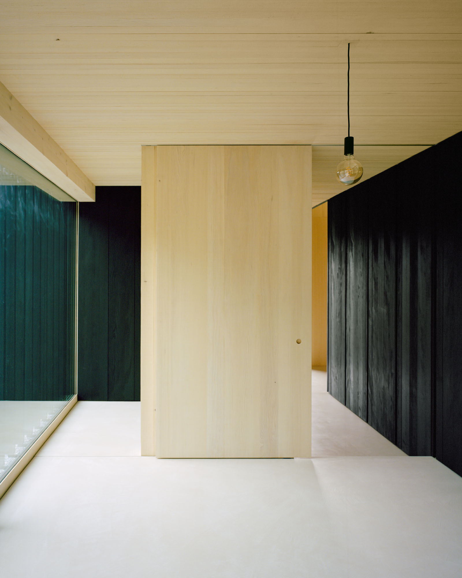 Plywood sliding door next to dark-stained timber paneling and a pendant light in the hallway