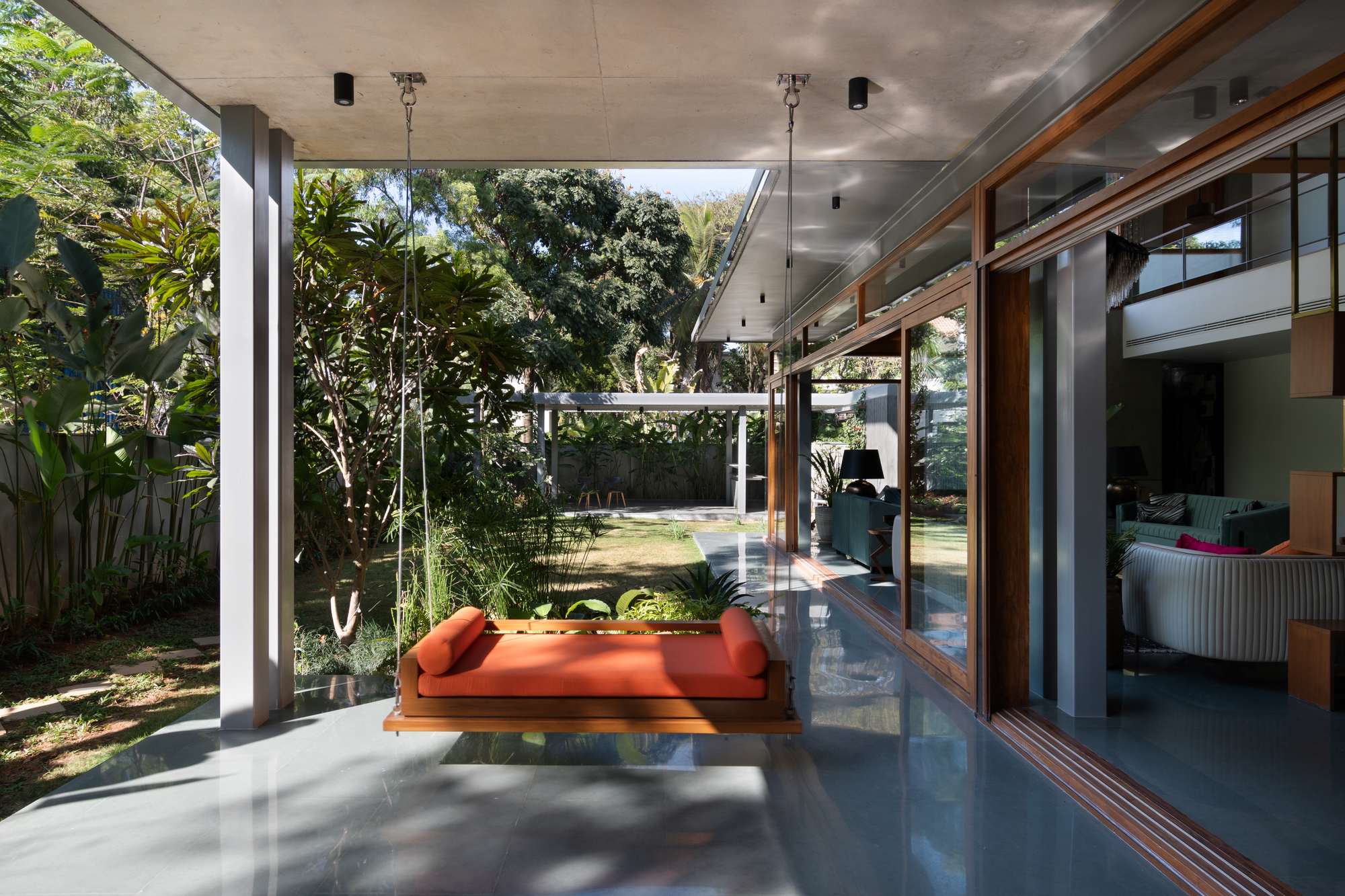 Covered terrace with suspended daybed overlooking garden through floor-to-ceiling sliding glass doors