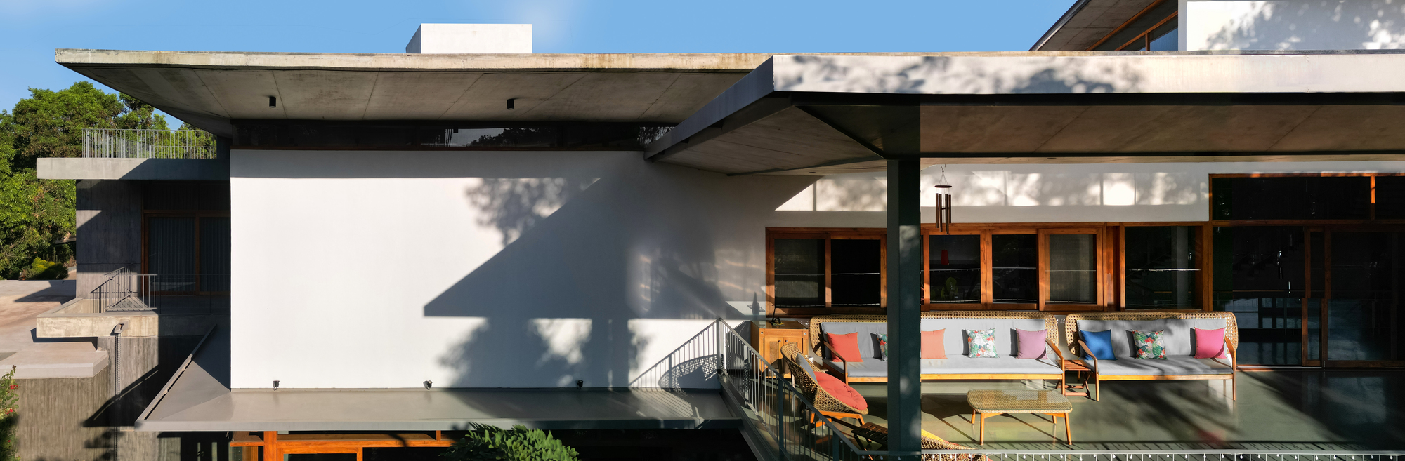 Cantilevered concrete roof over white stucco volumes with colorful lounge chairs on the upper deck