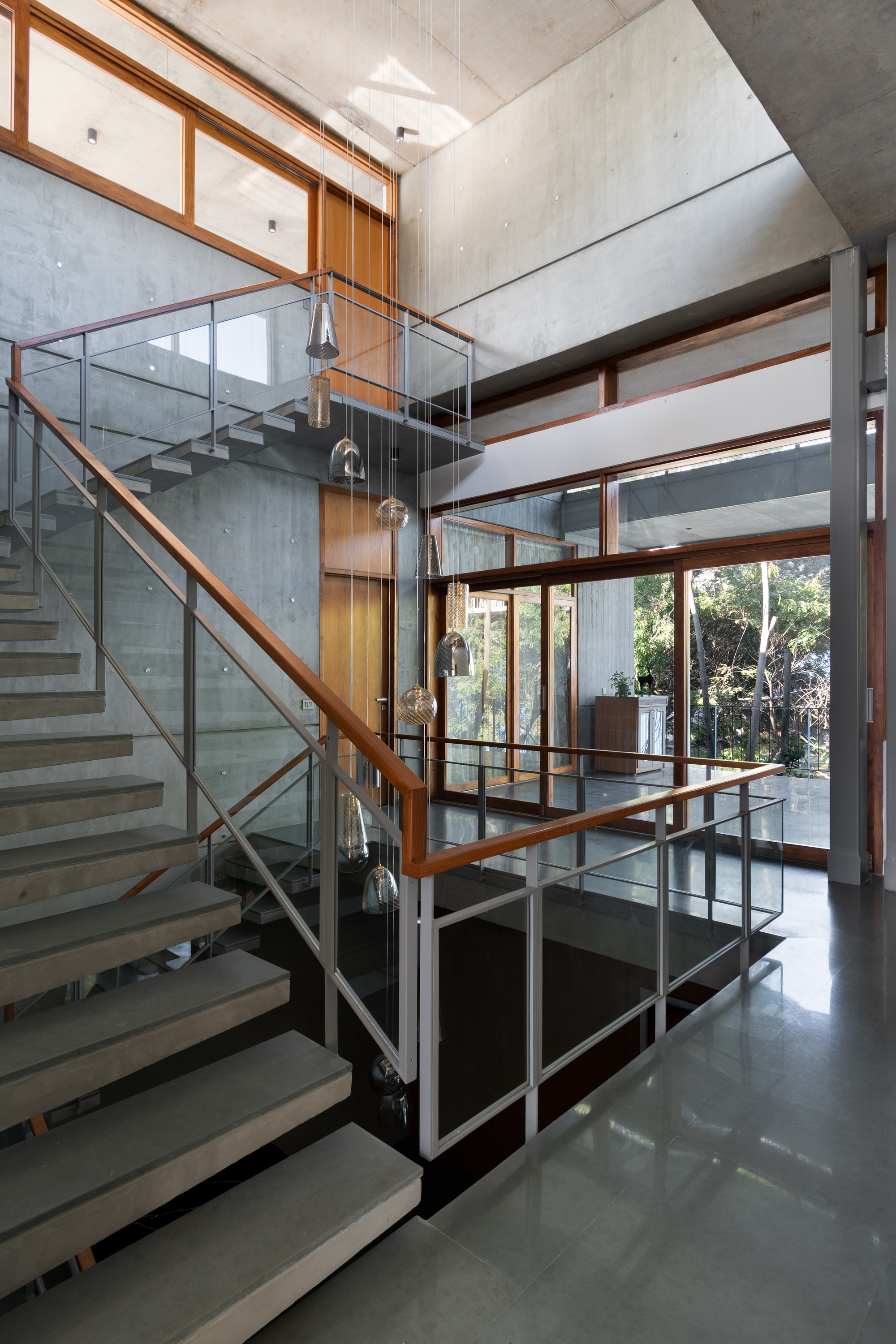 Central staircase with glass and timber railings linking split levels beneath exposed concrete ceilings