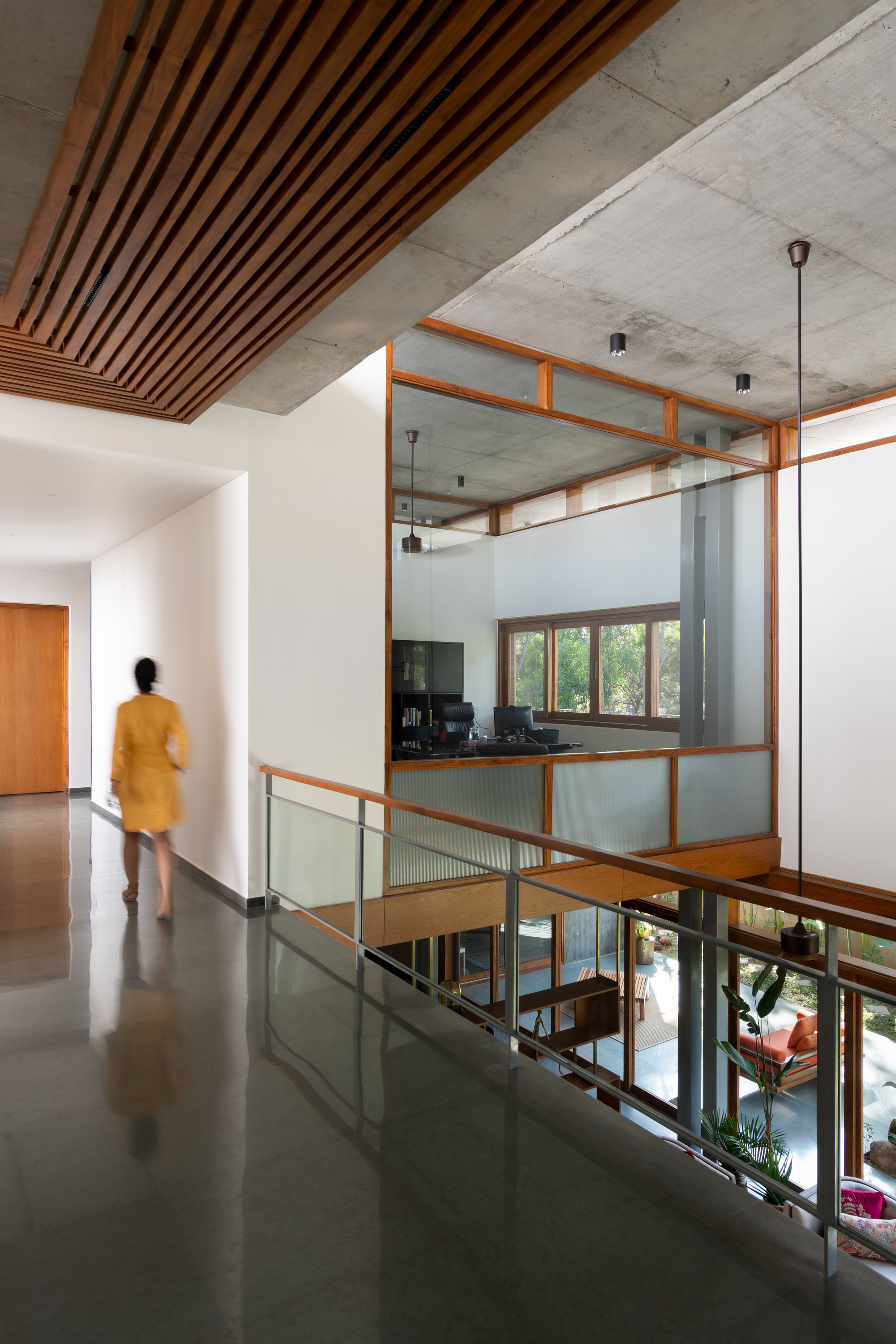 Upper level hallway with timber slat ceiling and glass-railed opening overlooking the double-height space below