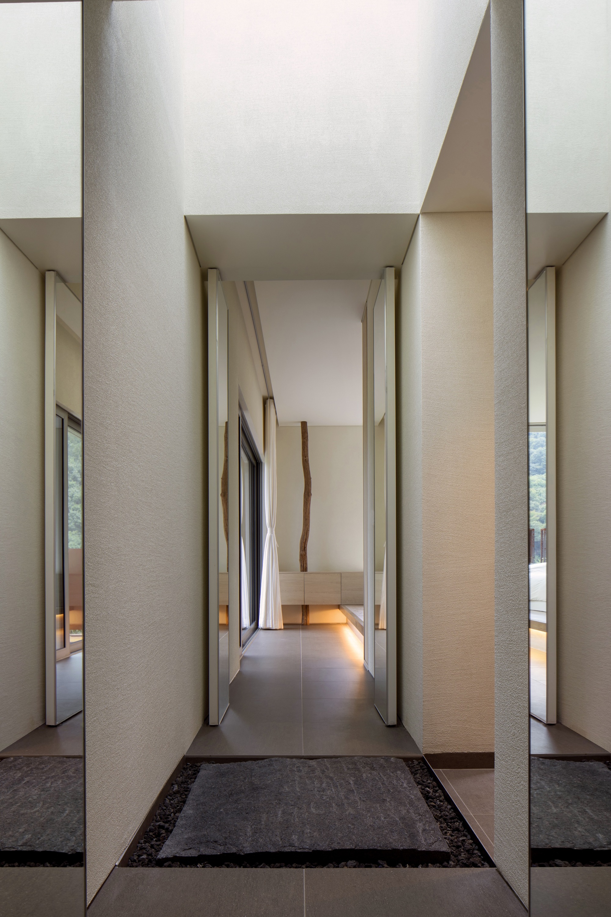 Corridor with slender recessed columns and angled wood-paneled walls leading to softly lit interior spaces