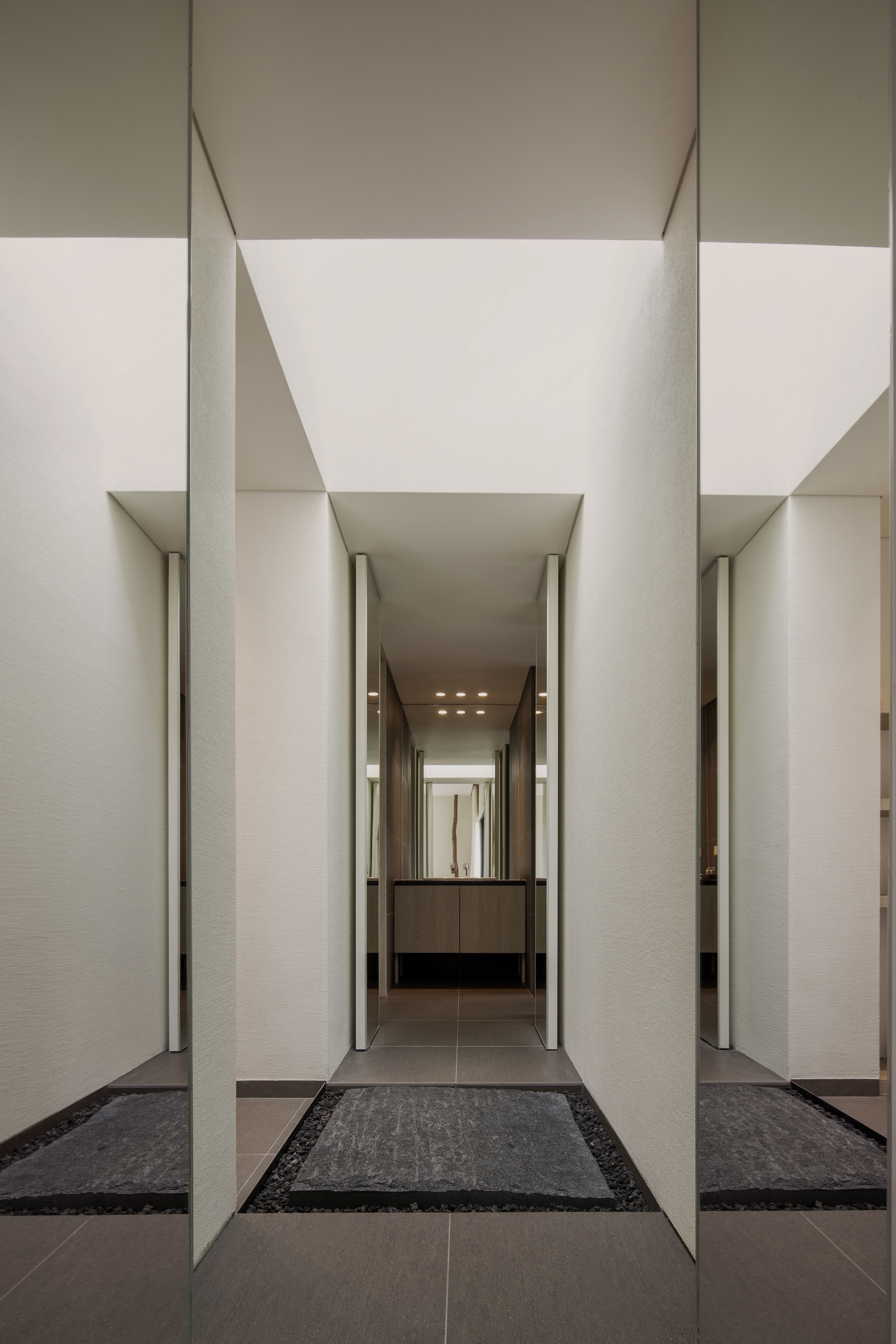 Recessed entry corridor with pale stone walls and dark floor tiles under linear ceiling beams