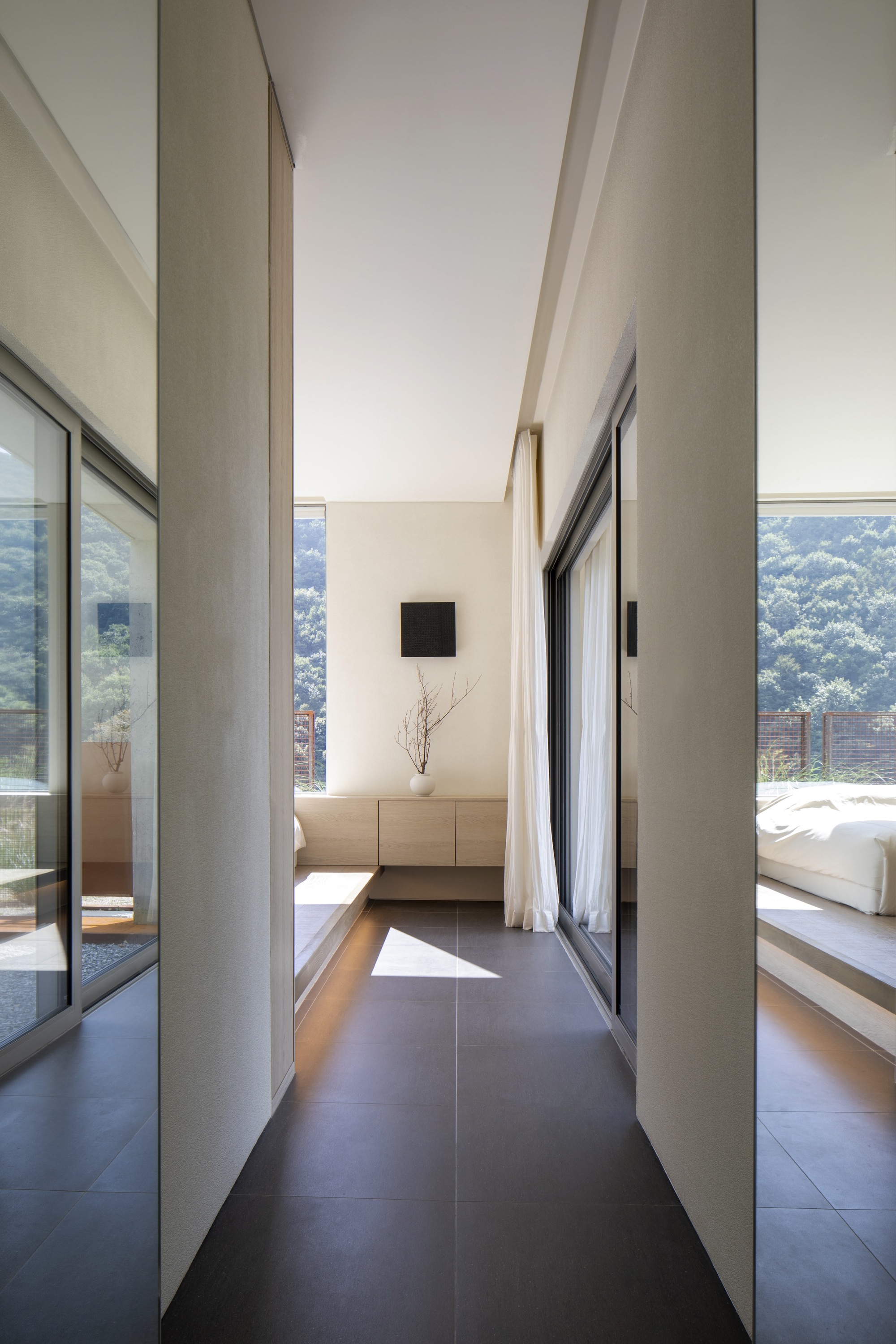Glazed hallway passage between concrete walls with daylight entering from bedroom and terrace beyond