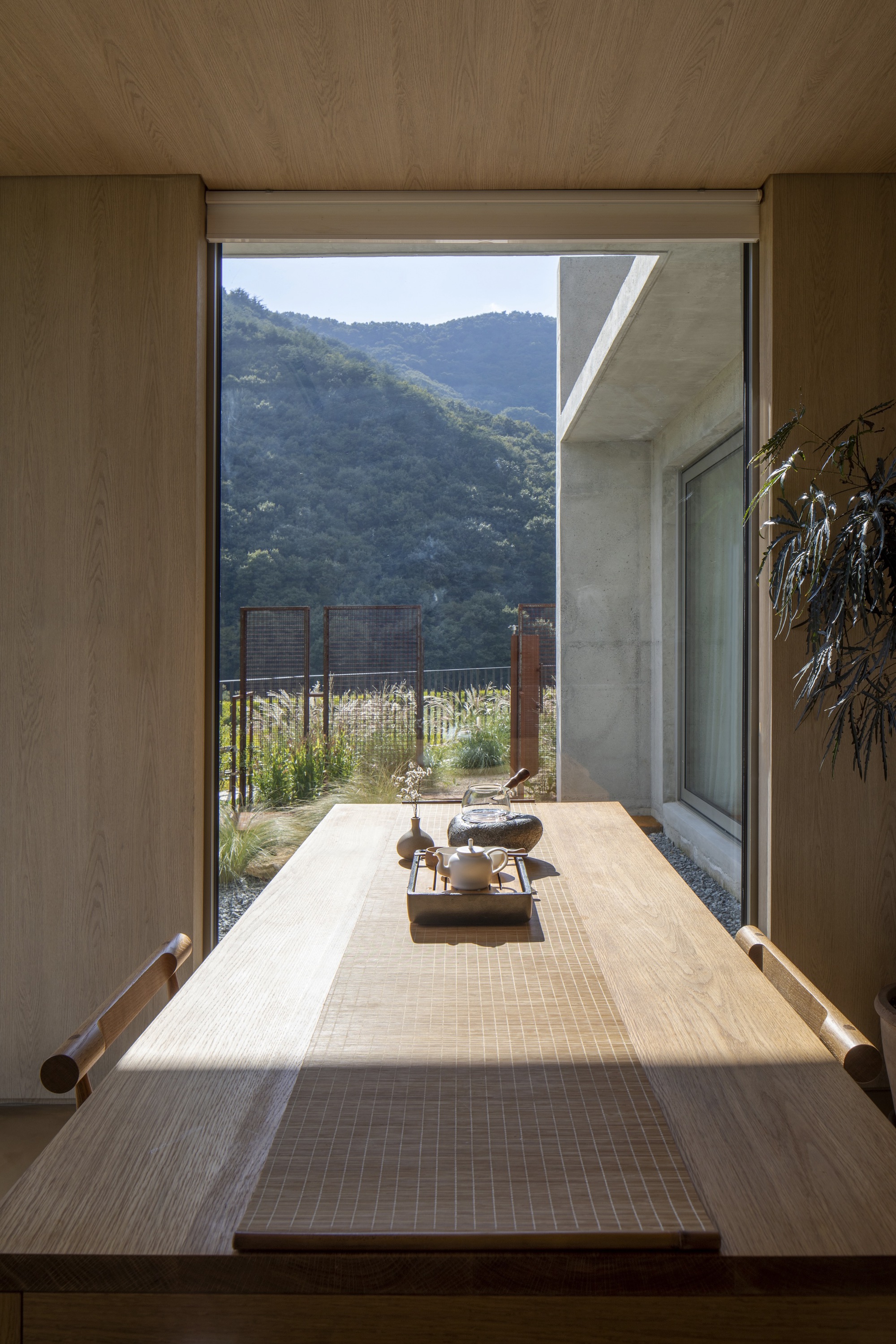 View through a timber-framed opening toward a planted courtyard with hills in the distance
