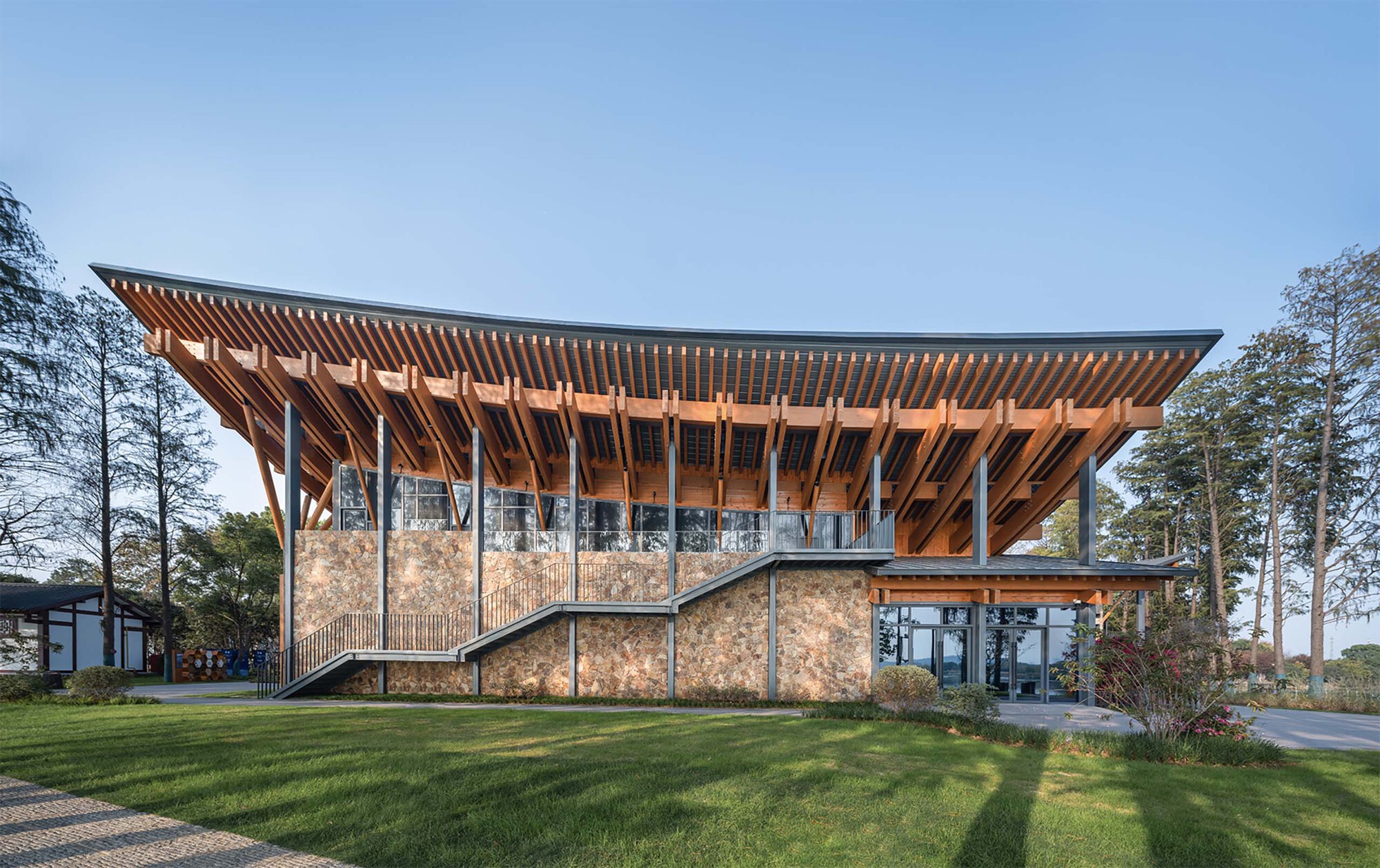 Timber-framed pavilion with exposed rafters and stone base walls on a grassy lawn at dusk