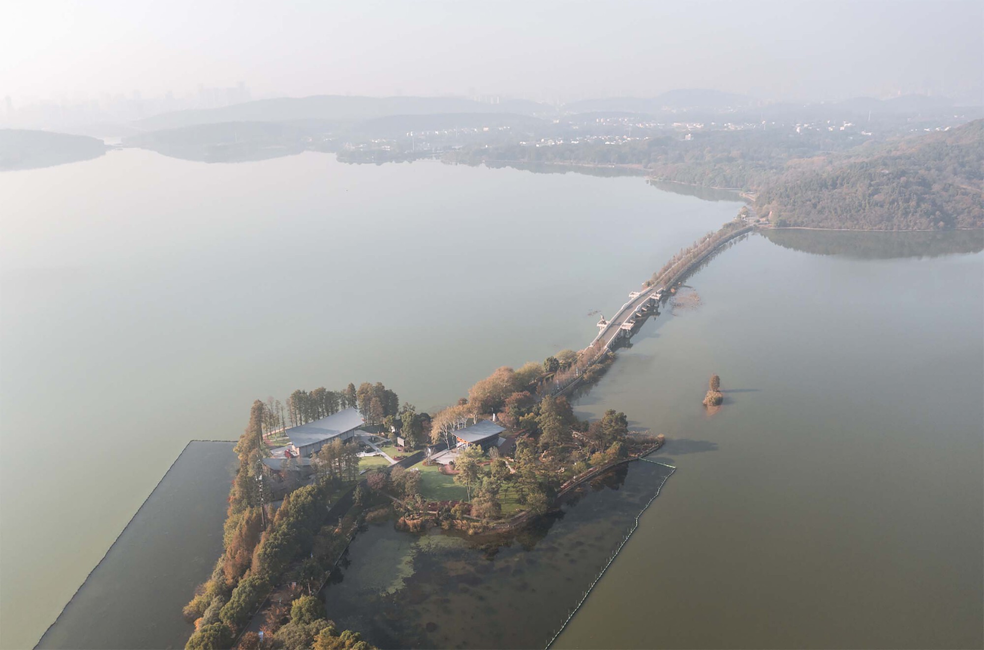 Aerial view of lakeside peninsula with buildings connected by causeway through misty water