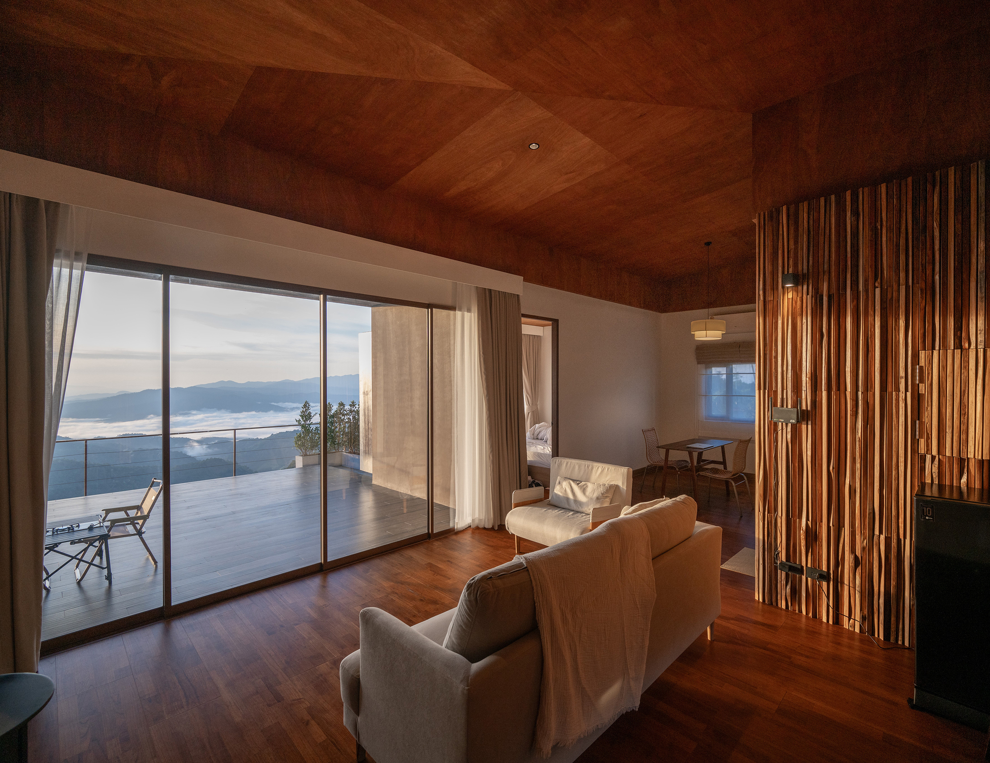 Living room with floor-to-ceiling glass doors opening to a terrace overlooking mountain ranges at twilight