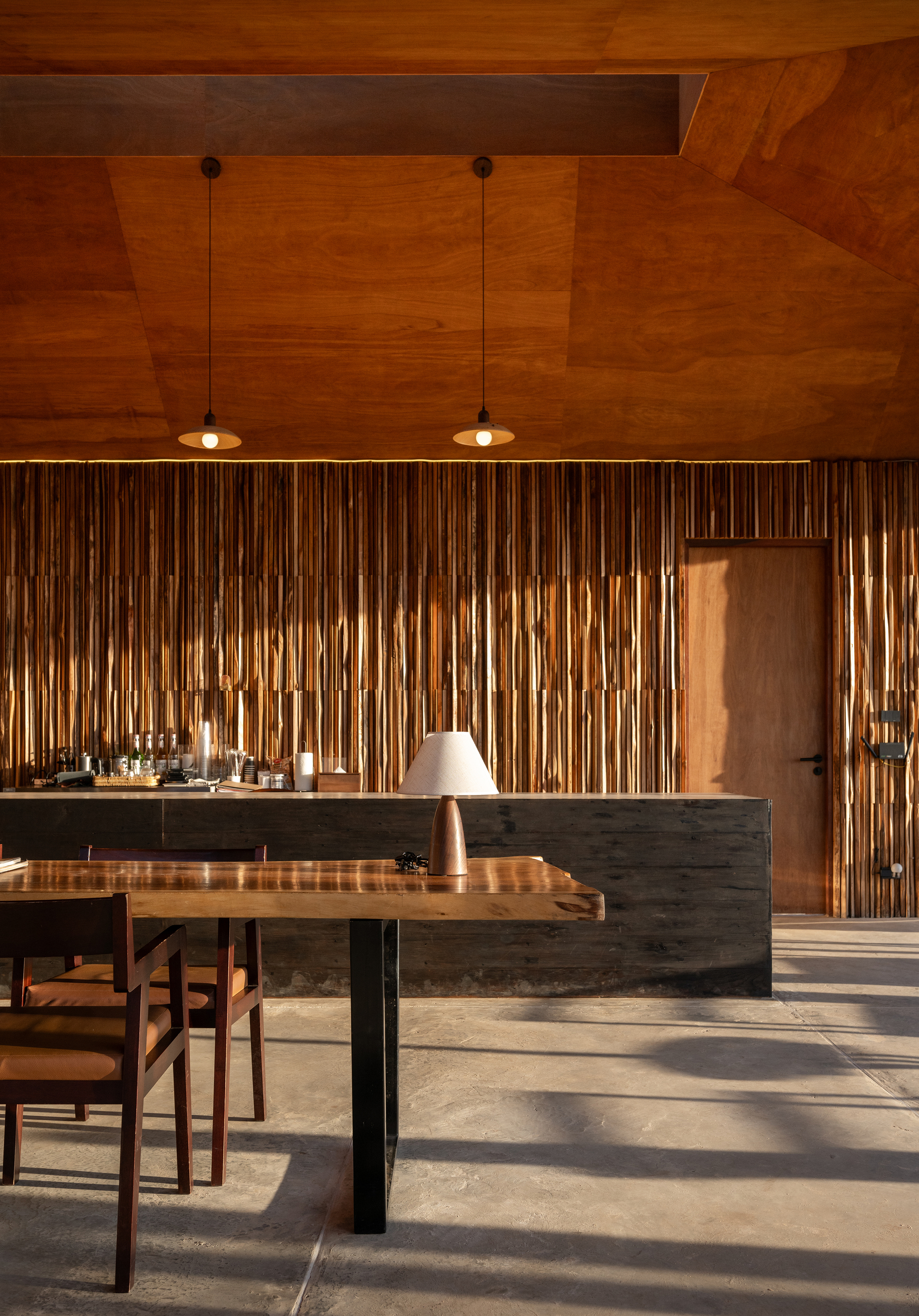 Kitchen island with dark stone base and timber dining table under warm pendant lights and geometric wood ceiling