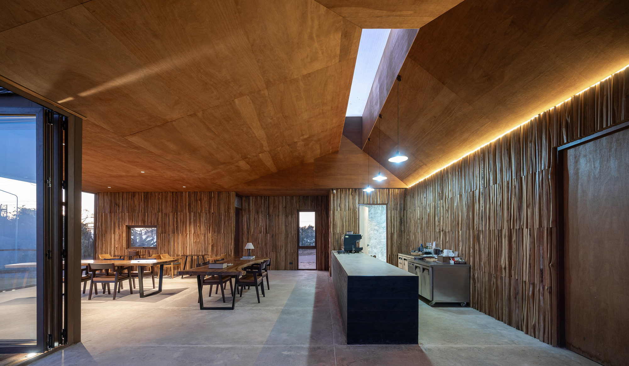 Open kitchen and dining area with concealed lighting, timber ceiling, and bifold doors at dusk