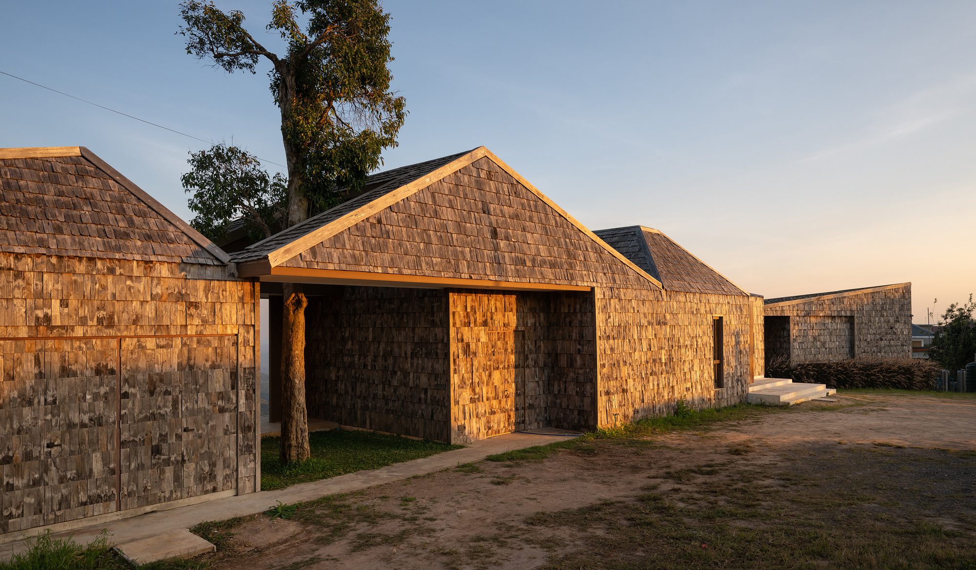 Cluster of gabled volumes clad in weathered wood shingles at golden hour