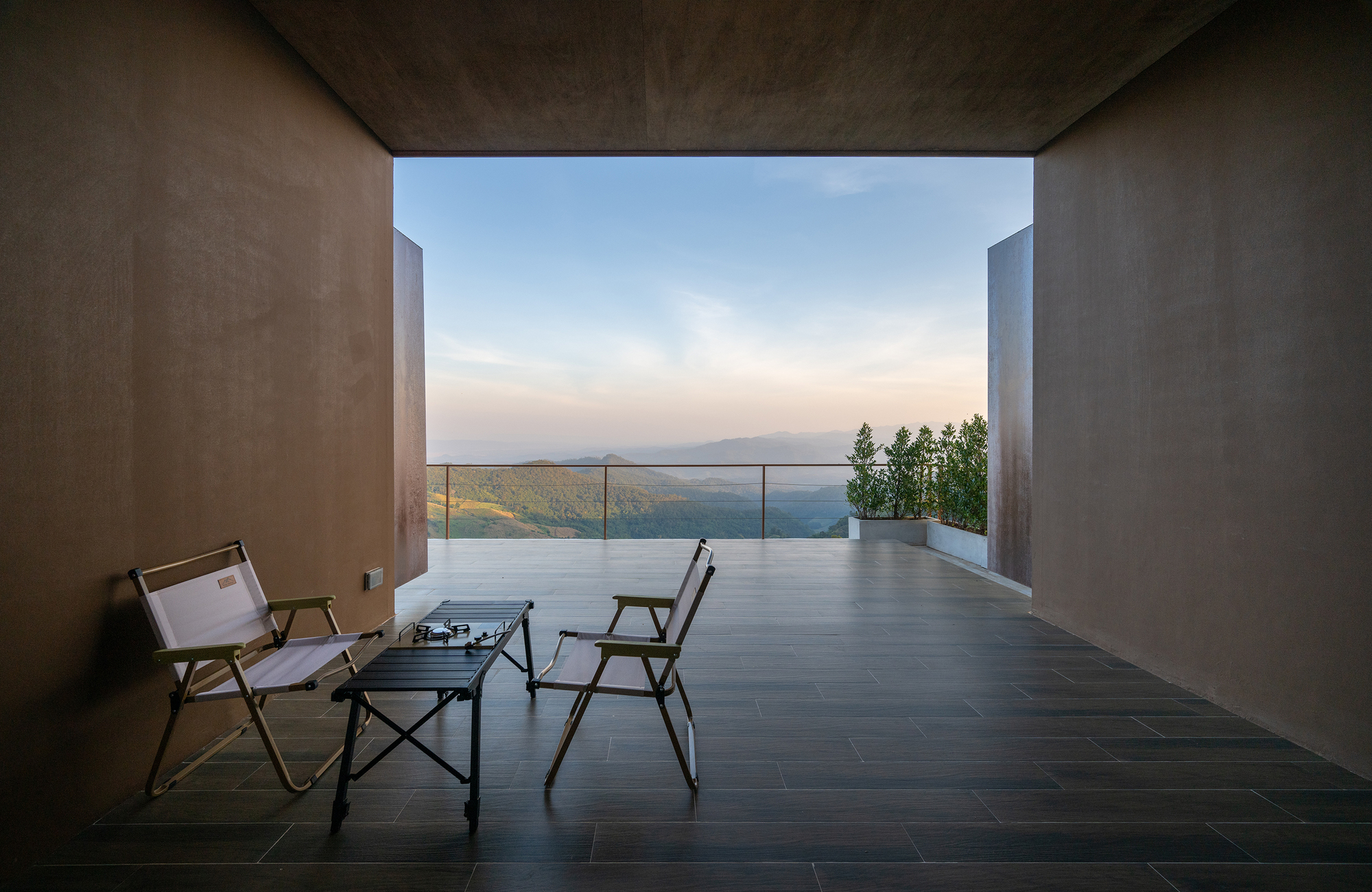 Covered terrace with dark stone flooring and two chairs overlooking rolling mountains through a wide opening