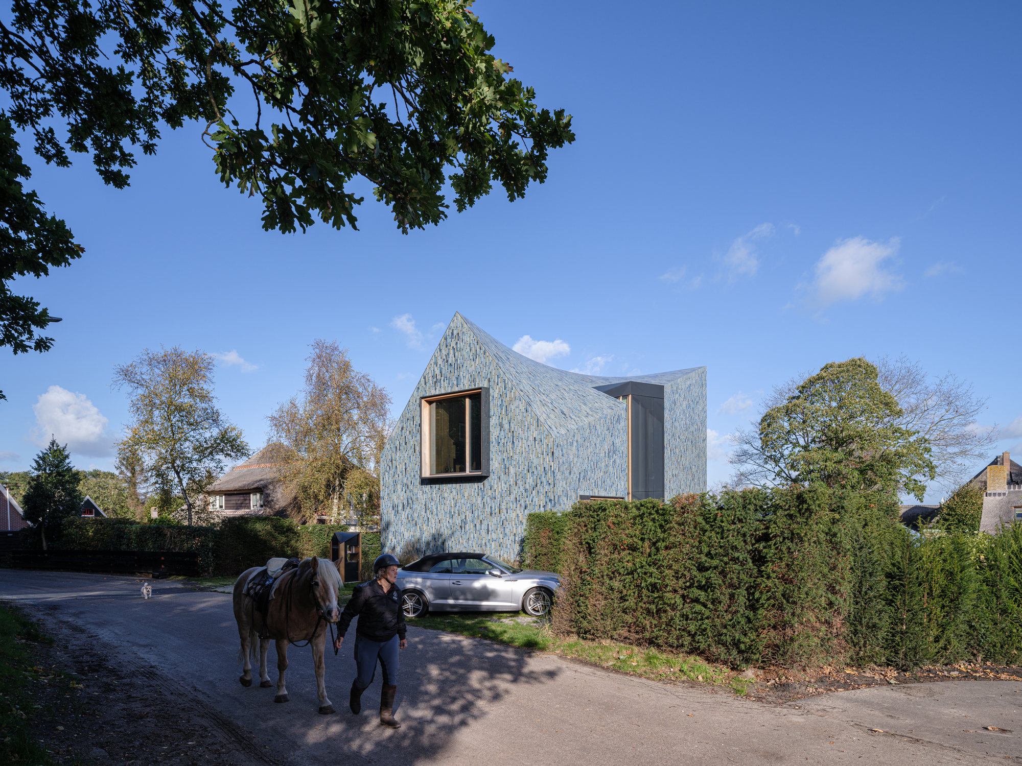 Person with horse passing the tile-clad facade along the residential street in autumn