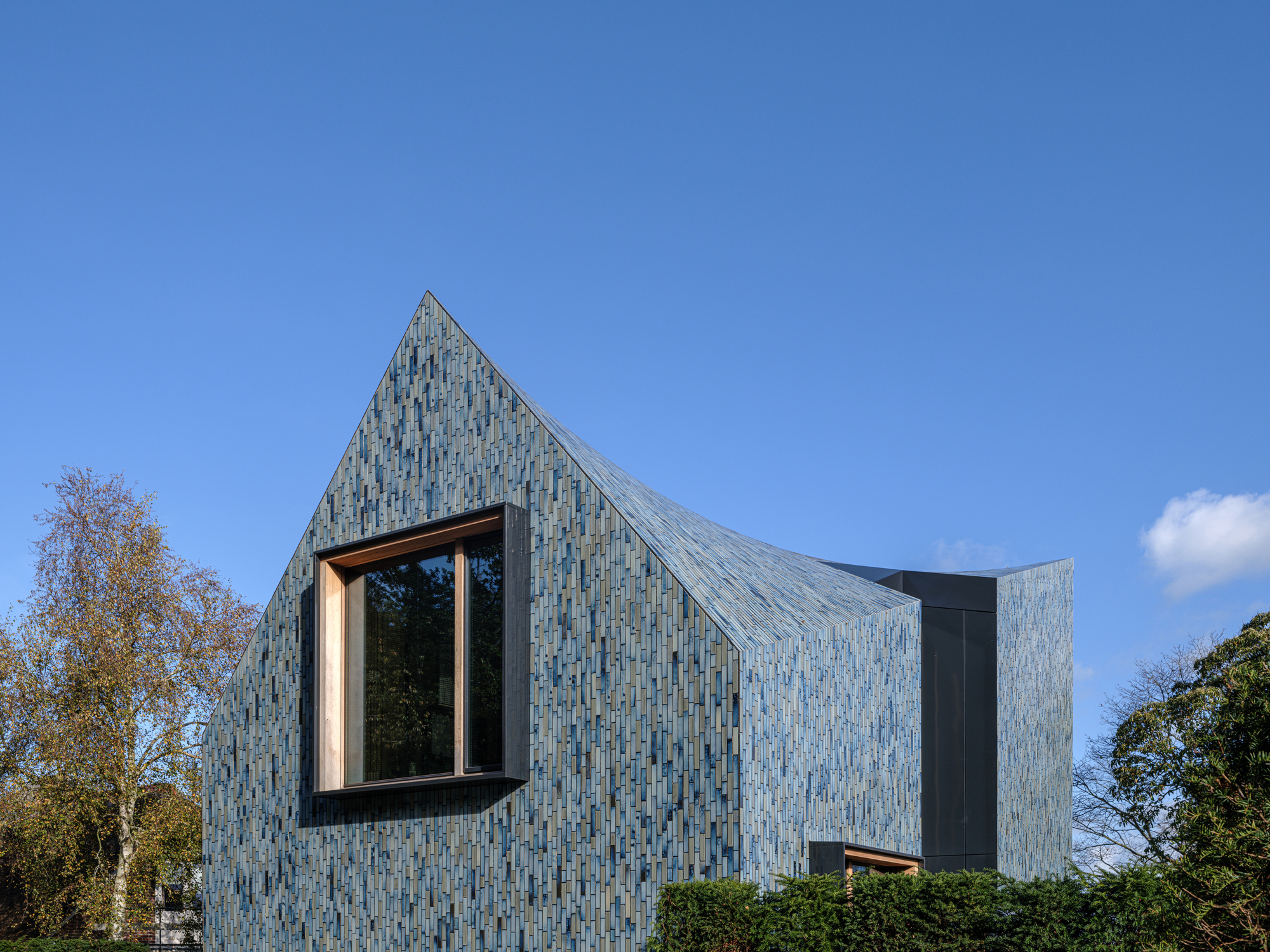Gabled facade showing the glazed ceramic tile cladding and projecting window frame against blue sky