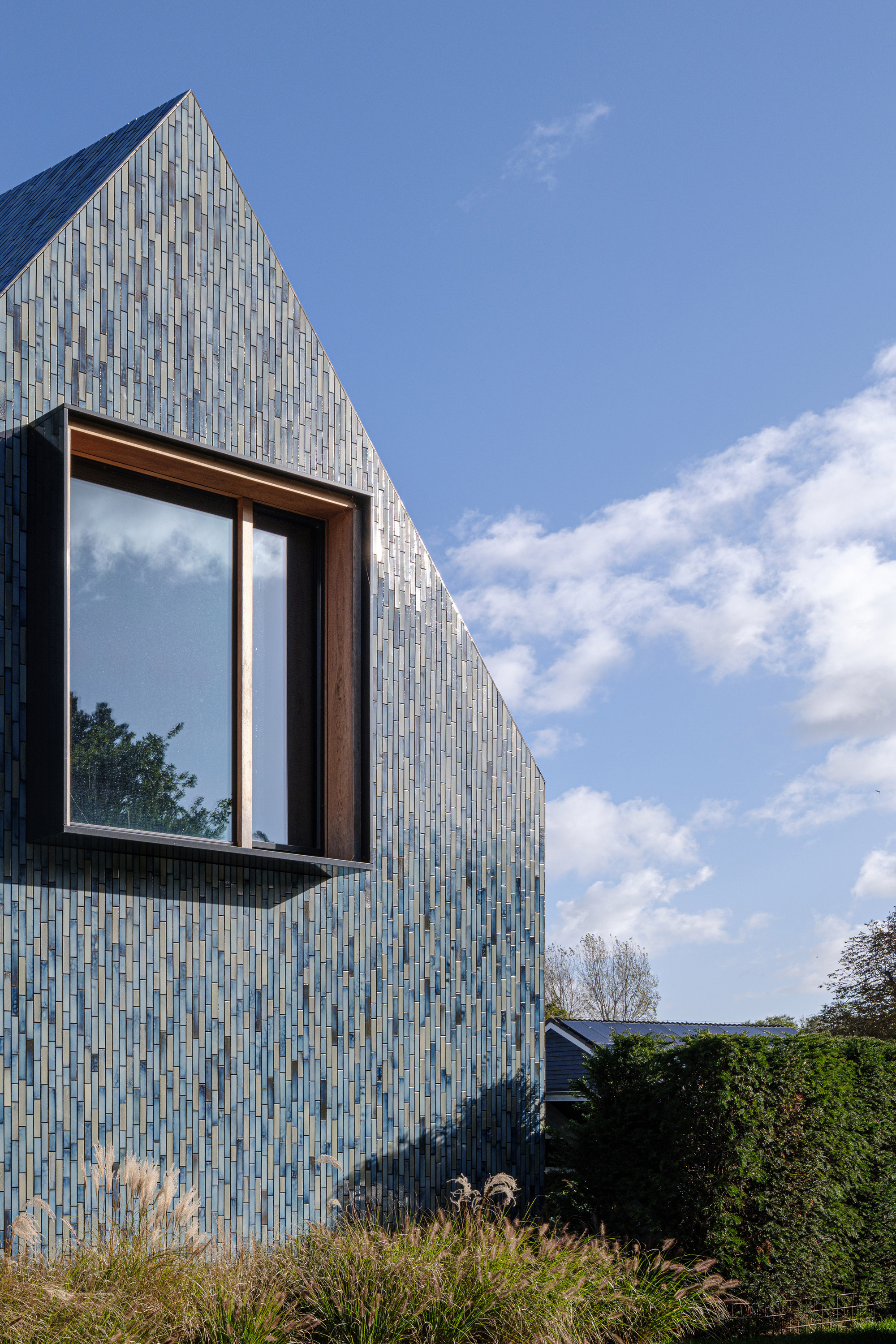 Projecting timber-framed window box set within the glazed tile facade under scattered clouds
