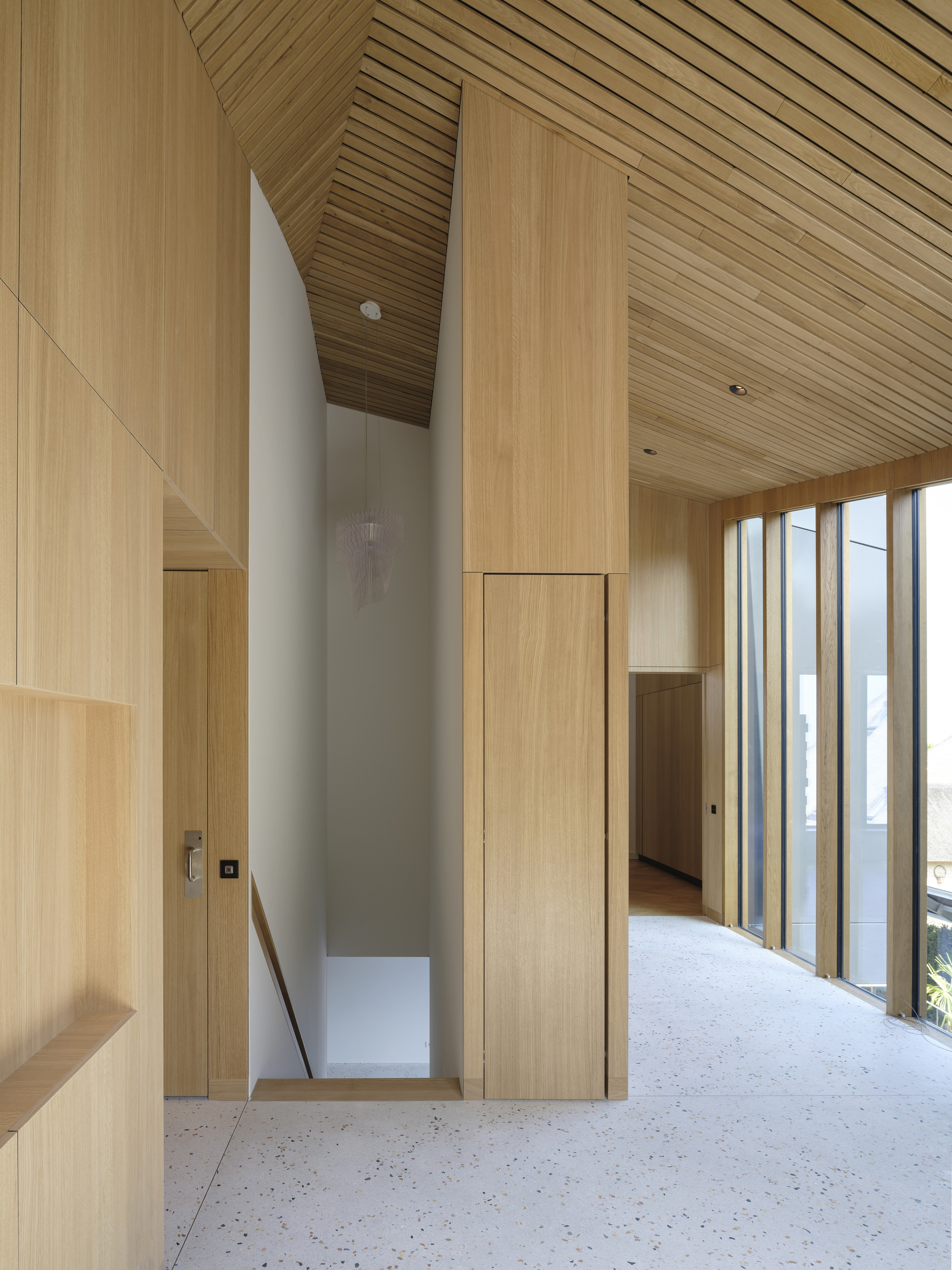 Interior hallway with timber-clad walls and slat ceiling overlooking a double-height void