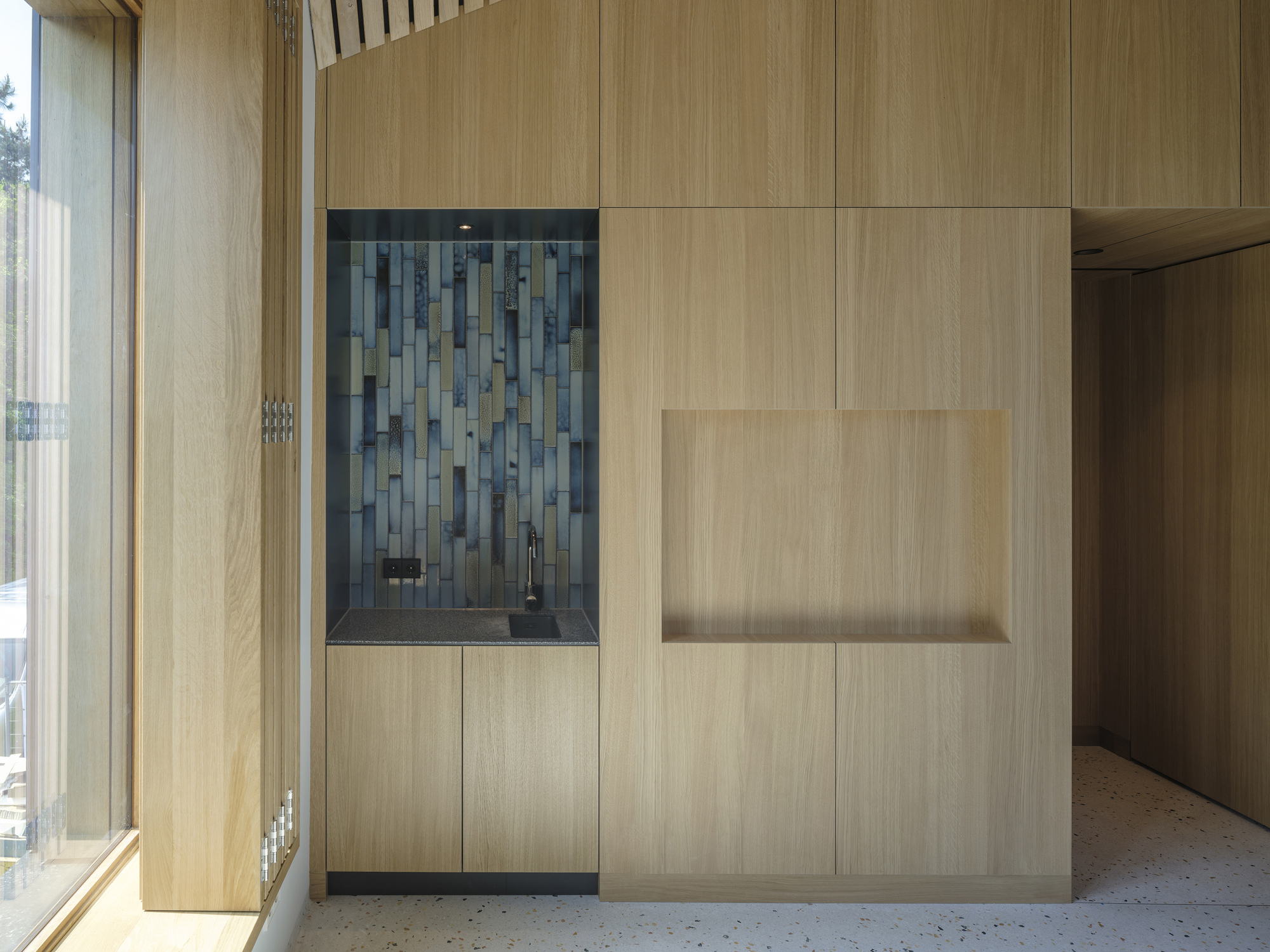Built-in cabinetry with blue tile backsplash niche set within light wood paneling